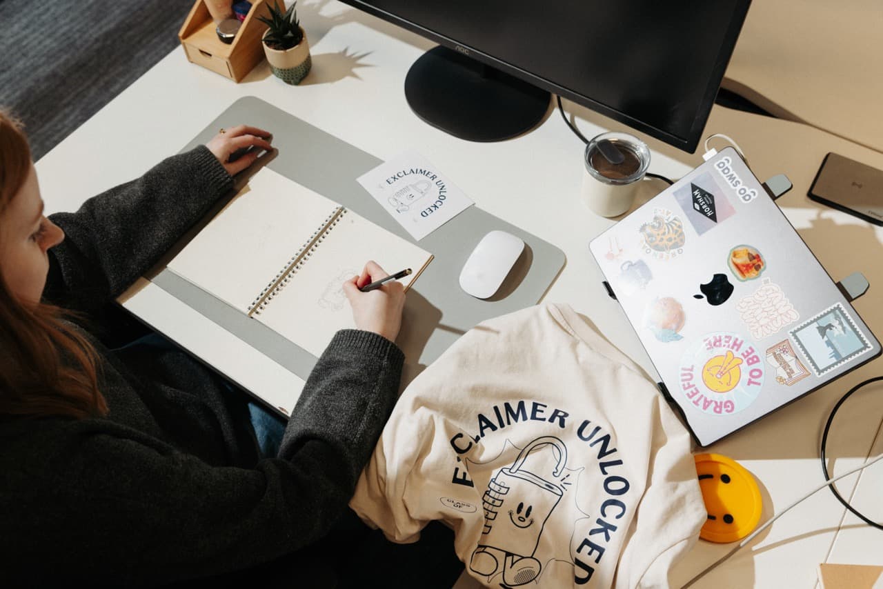 A Go Swag designer sketching concepts next to a branded sweatshirt and laptop