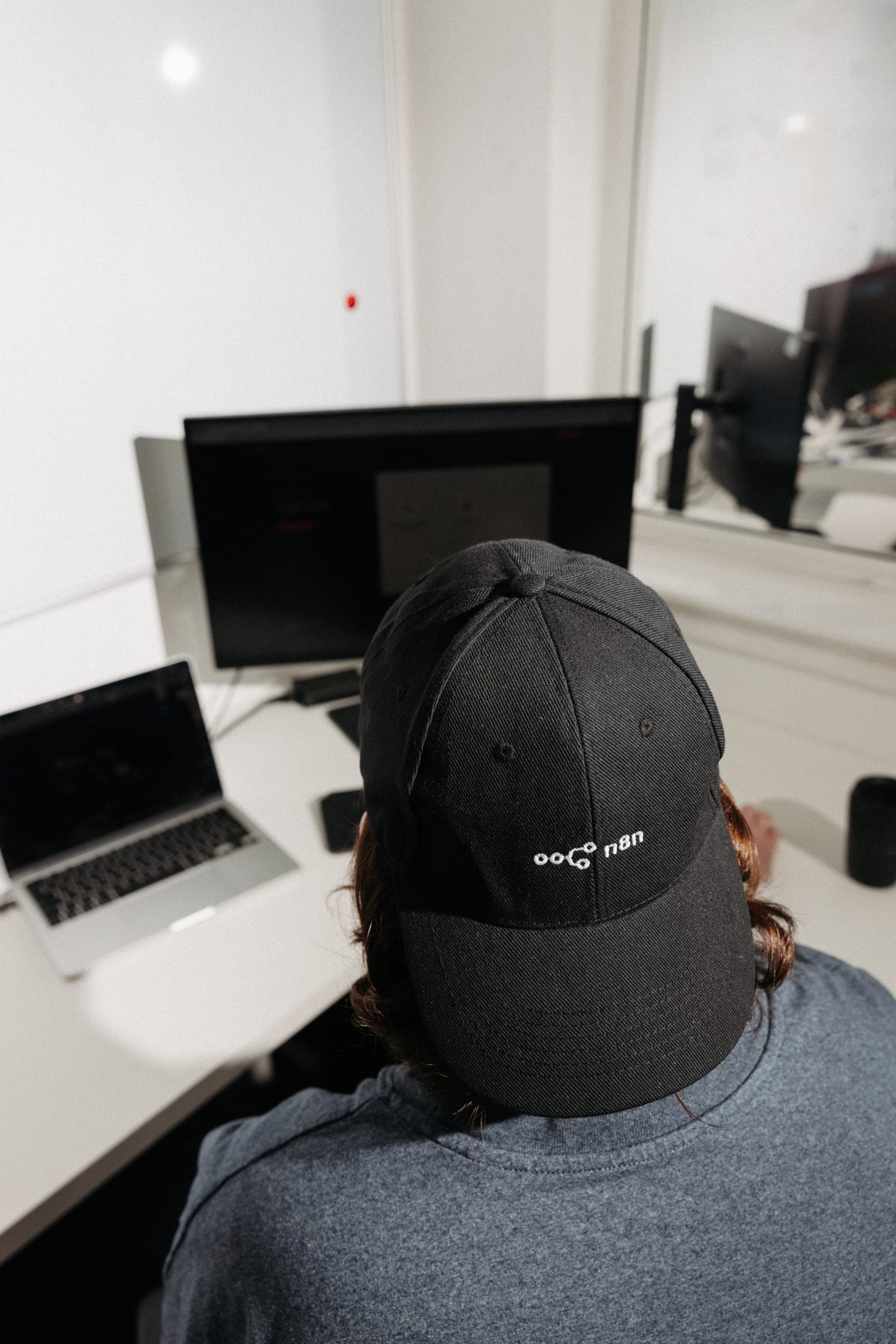 Over-the-shoulder view of a person in a black n8n cap at a desk