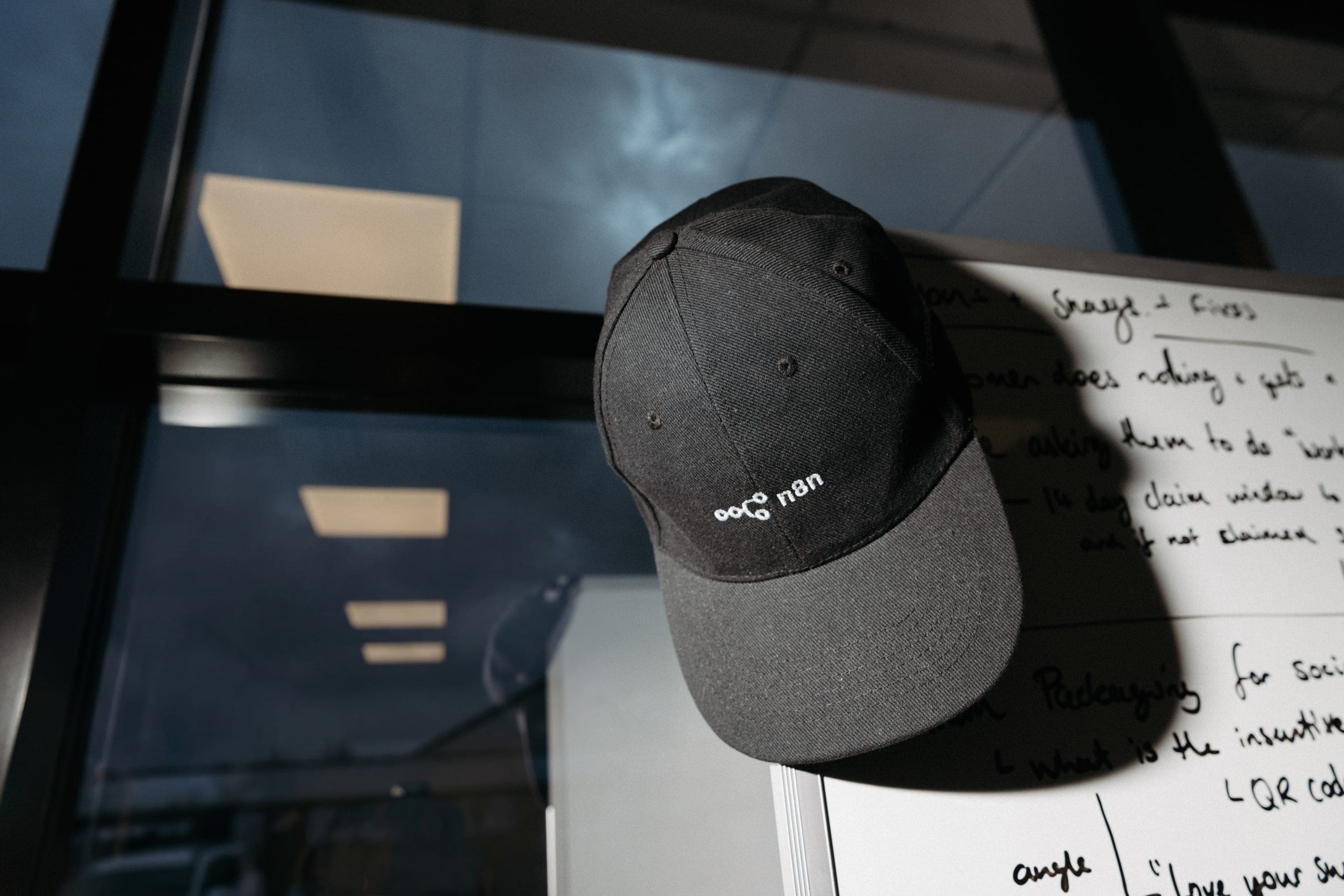 Black n8n cap hanging on the corner of a whiteboard with handwritten notes