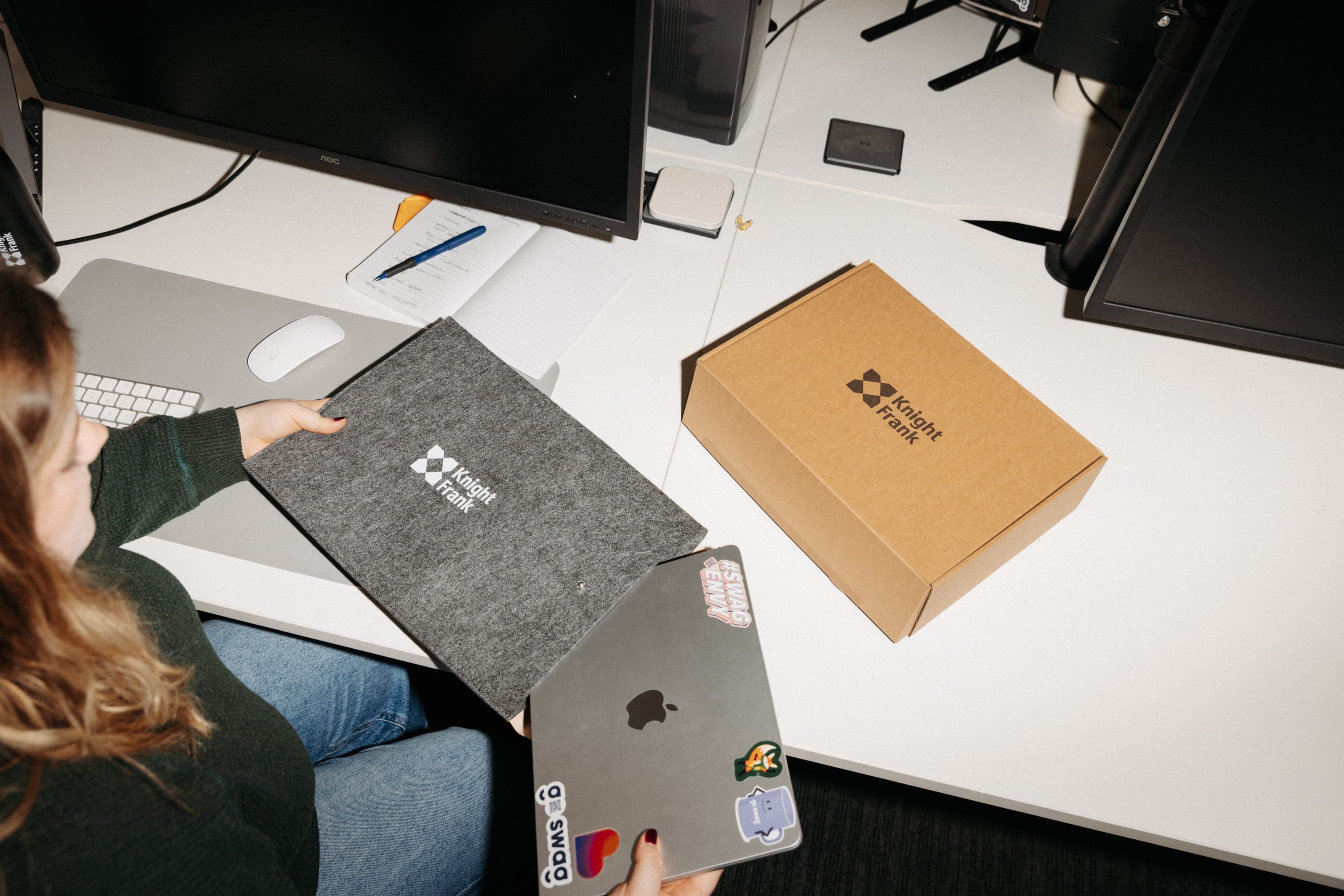 A woman holds a grey felt Knight Frank laptop sleeve beside a kraft box printed with the Knight Frank logo