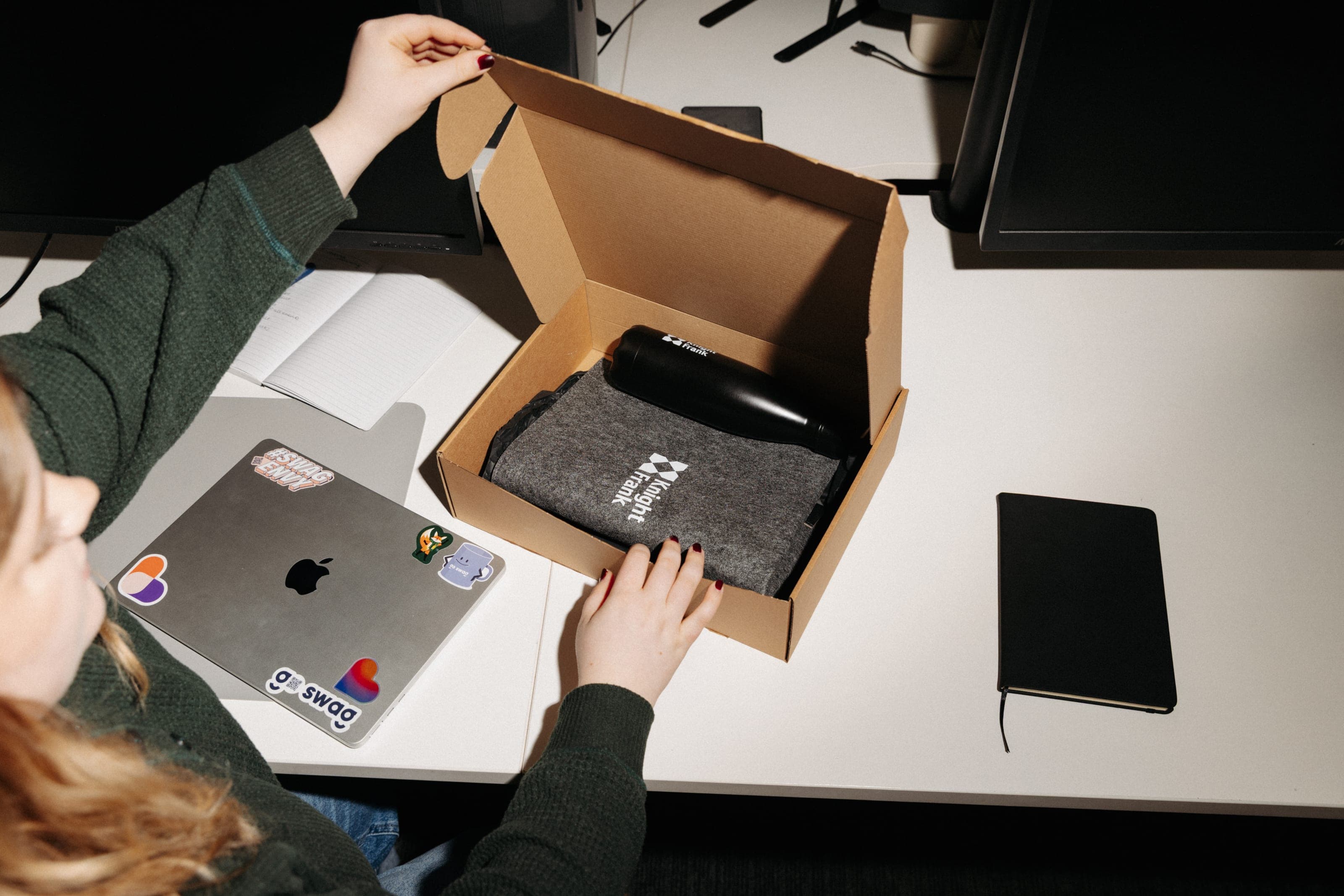 Woman opening a kraft box holding a grey felt Knight Frank sleeve and a black branded bottle