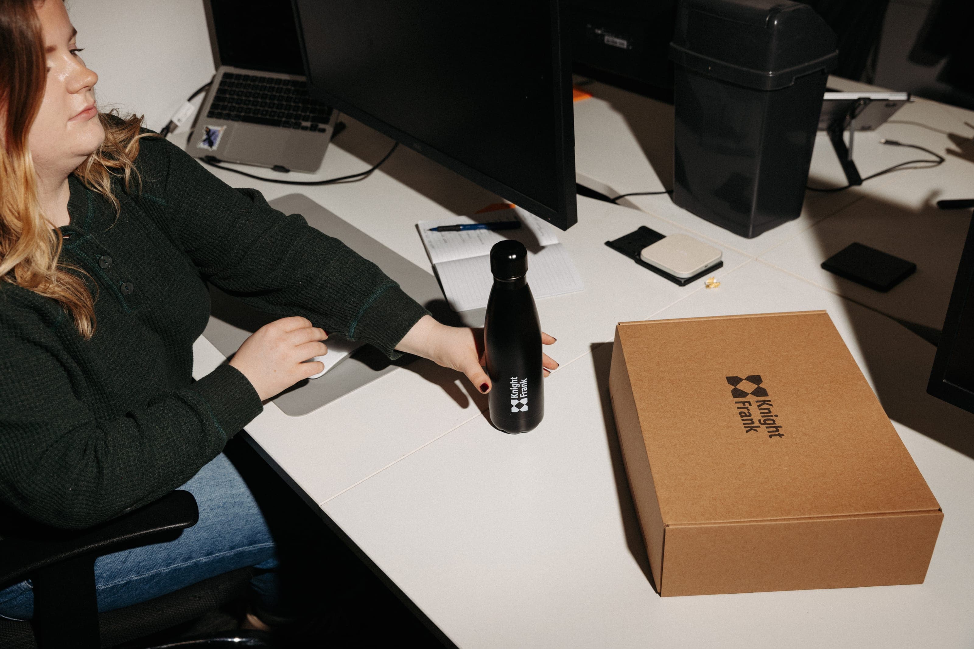 A woman at her desk with a black Knight Frank bottle beside a closed Knight Frank kraft box