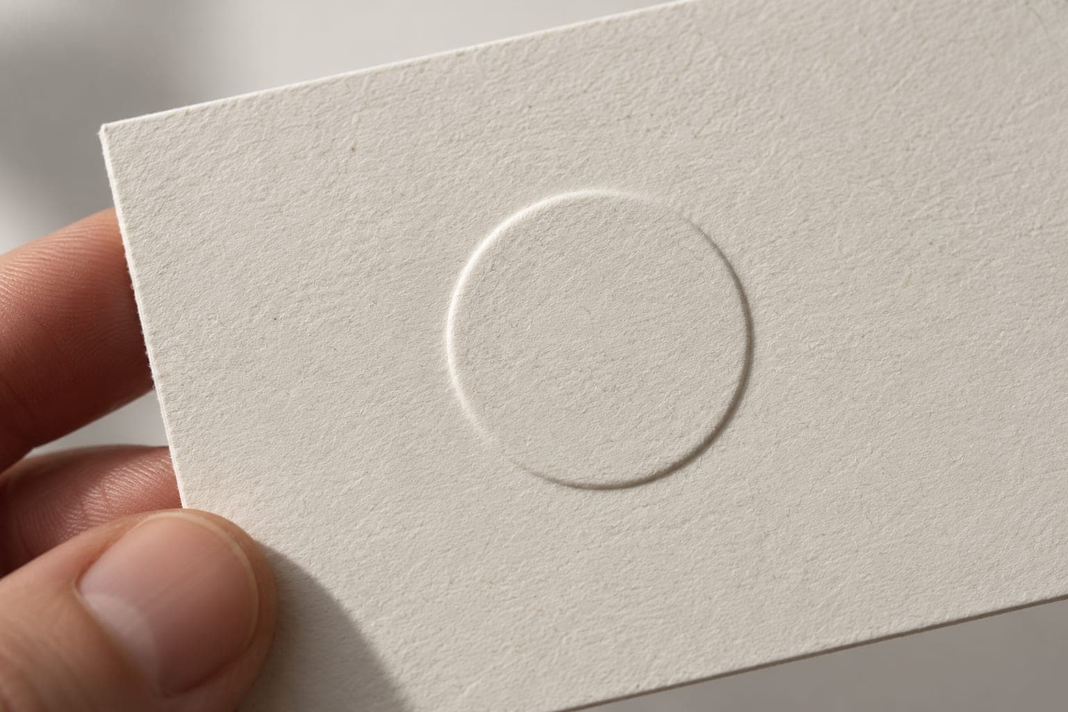 Fingers holding a cream card with a blind-embossed circle