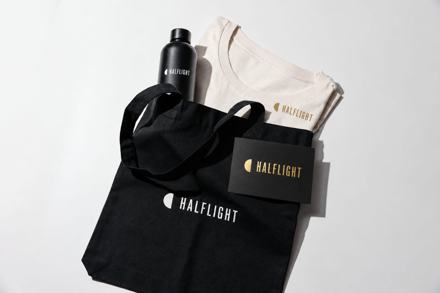 A black tote, black bottle, cream T-shirt and black card, all printed with the same film-title logo, laid out as a premiere gift kit