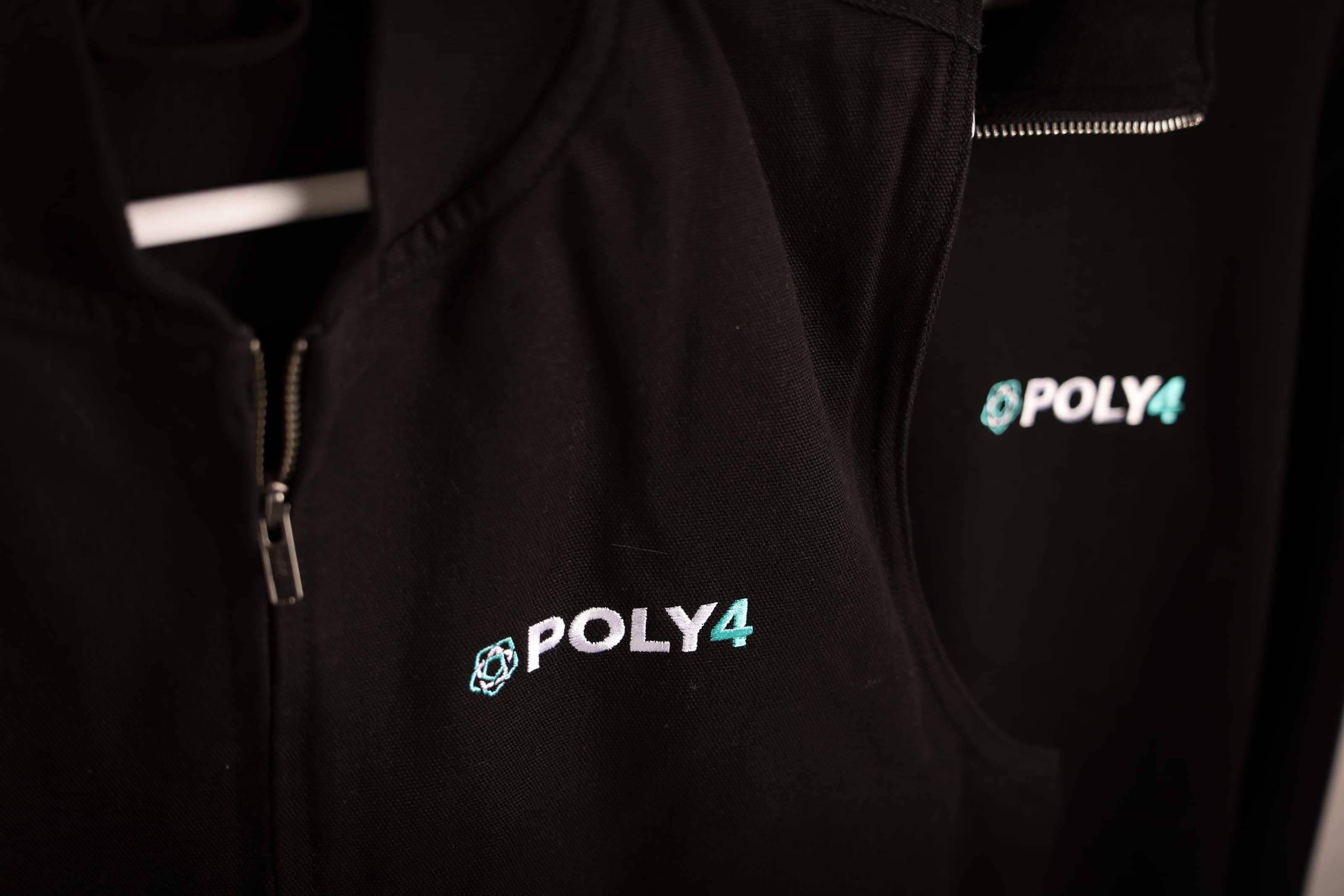 Close-up of white and teal POLY4 embroidery on a black zip gilet