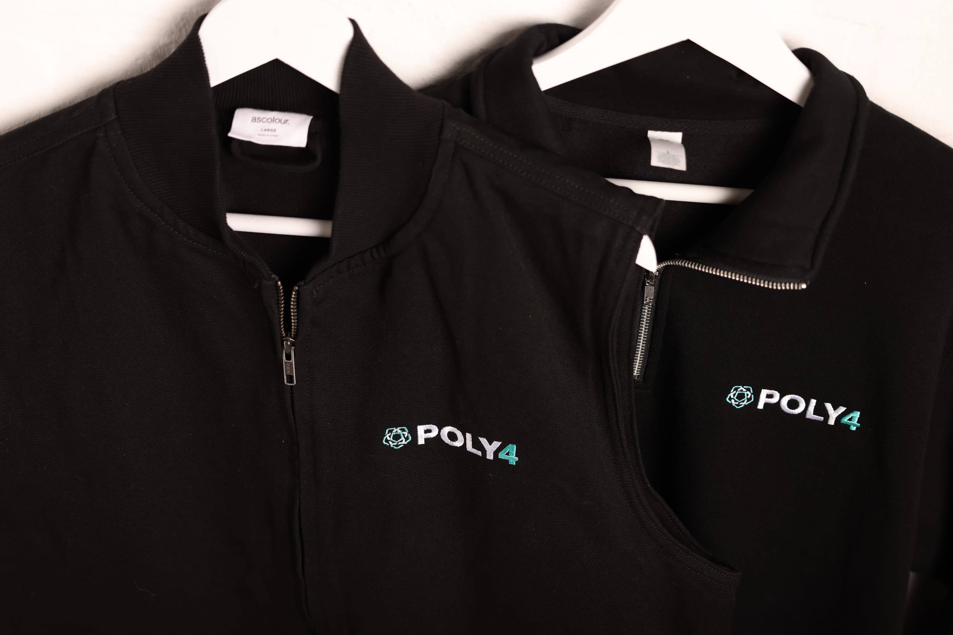 Two black POLY4-embroidered garments on white hangers