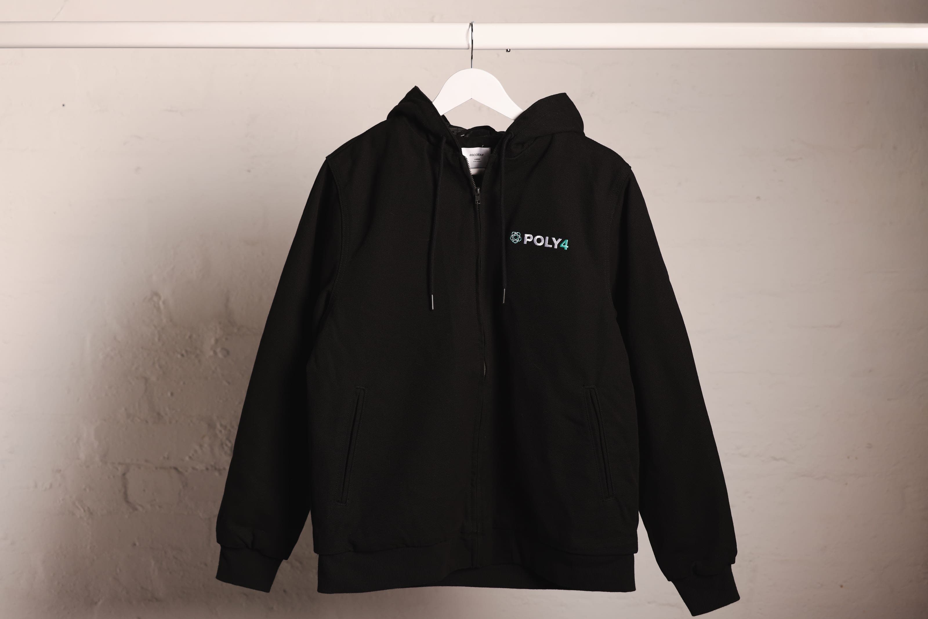 A black hooded zip work jacket with POLY4 chest embroidery on a white rail