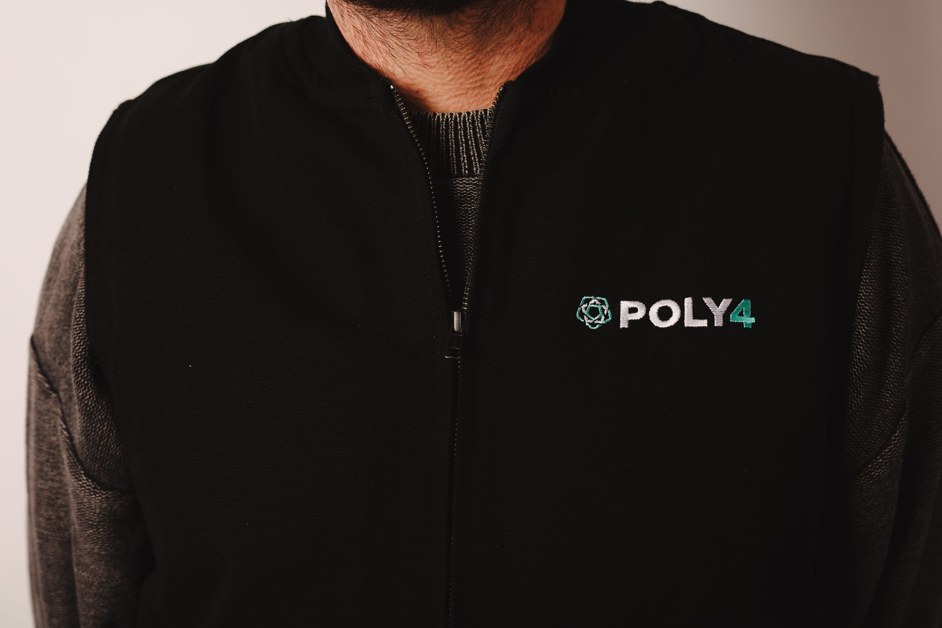 Torso of a man wearing a black zip gilet embroidered with the POLY4 logo over a grey knit