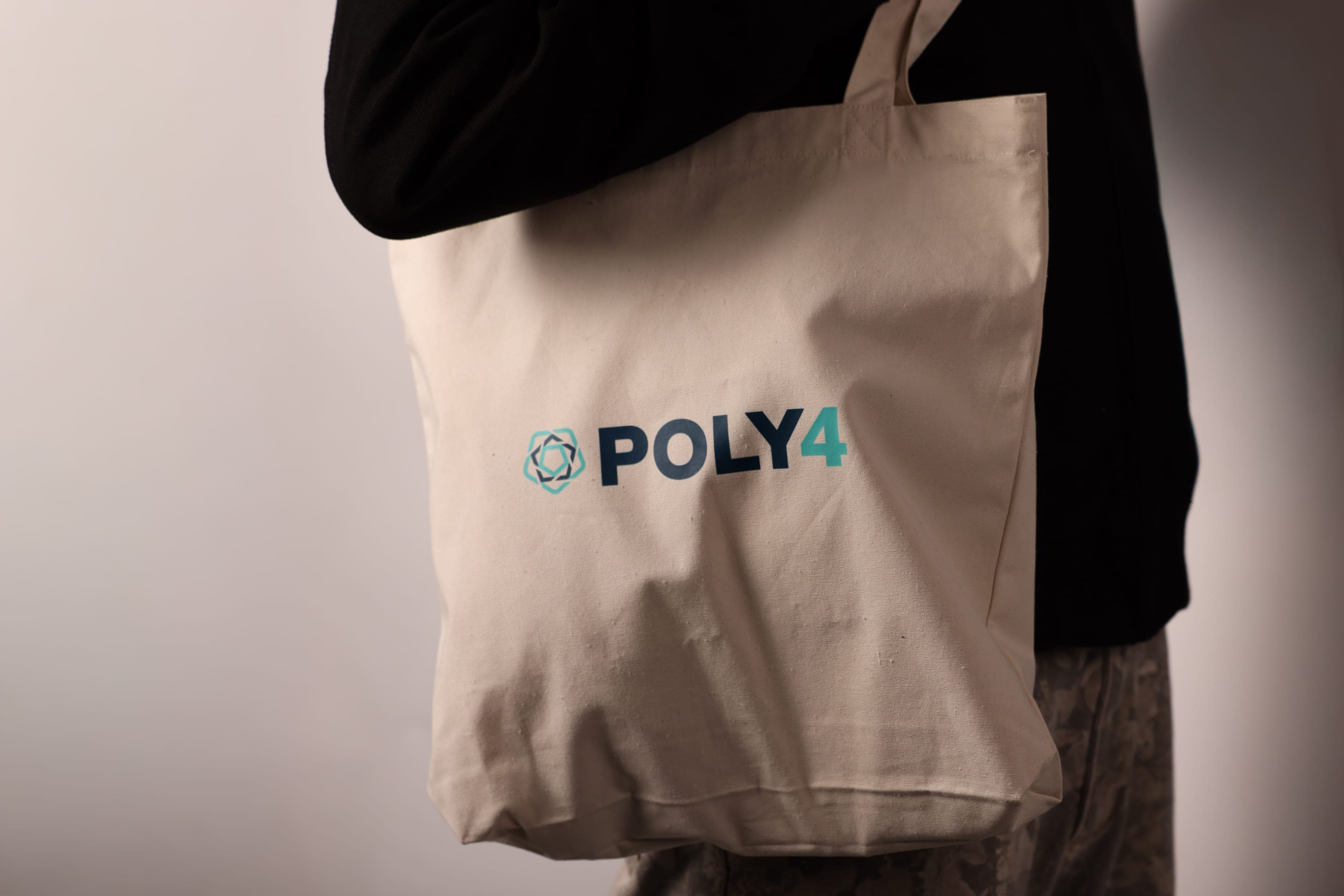 A natural canvas tote printed with the POLY4 logo carried on a shoulder
