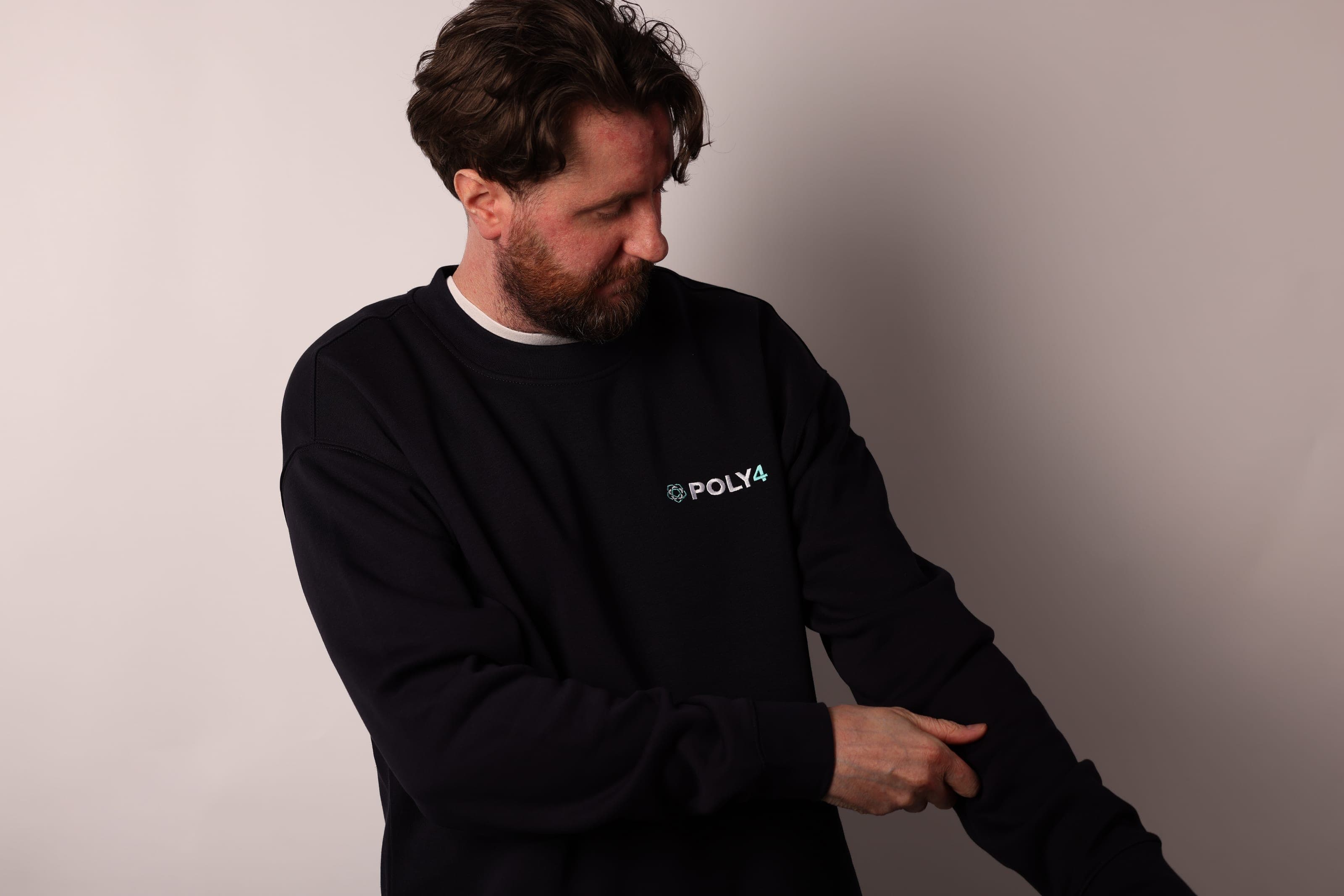 Bearded man in a black POLY4 sweatshirt adjusting his sleeve