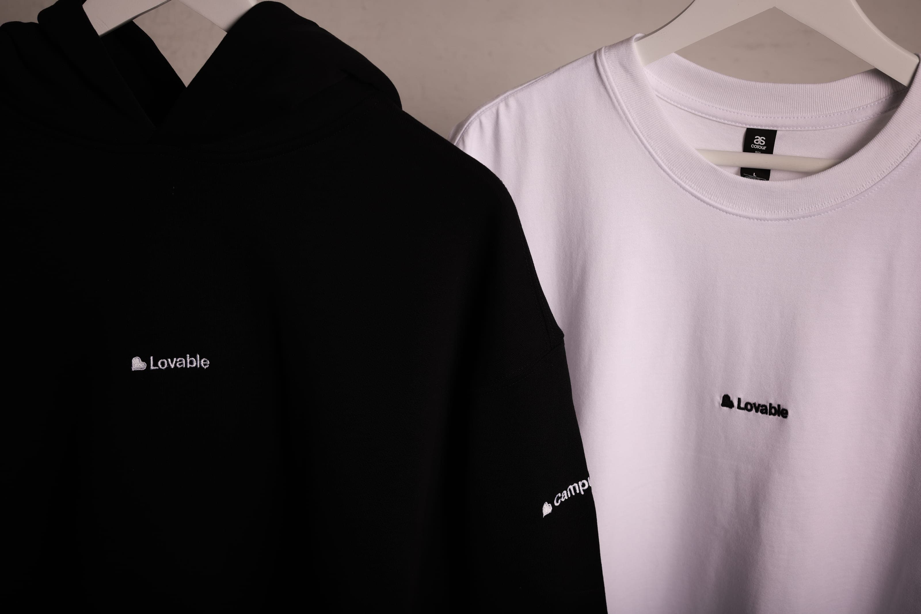 A black hoodie and a white T-shirt on hangers, each with small Lovable embroidery on the chest