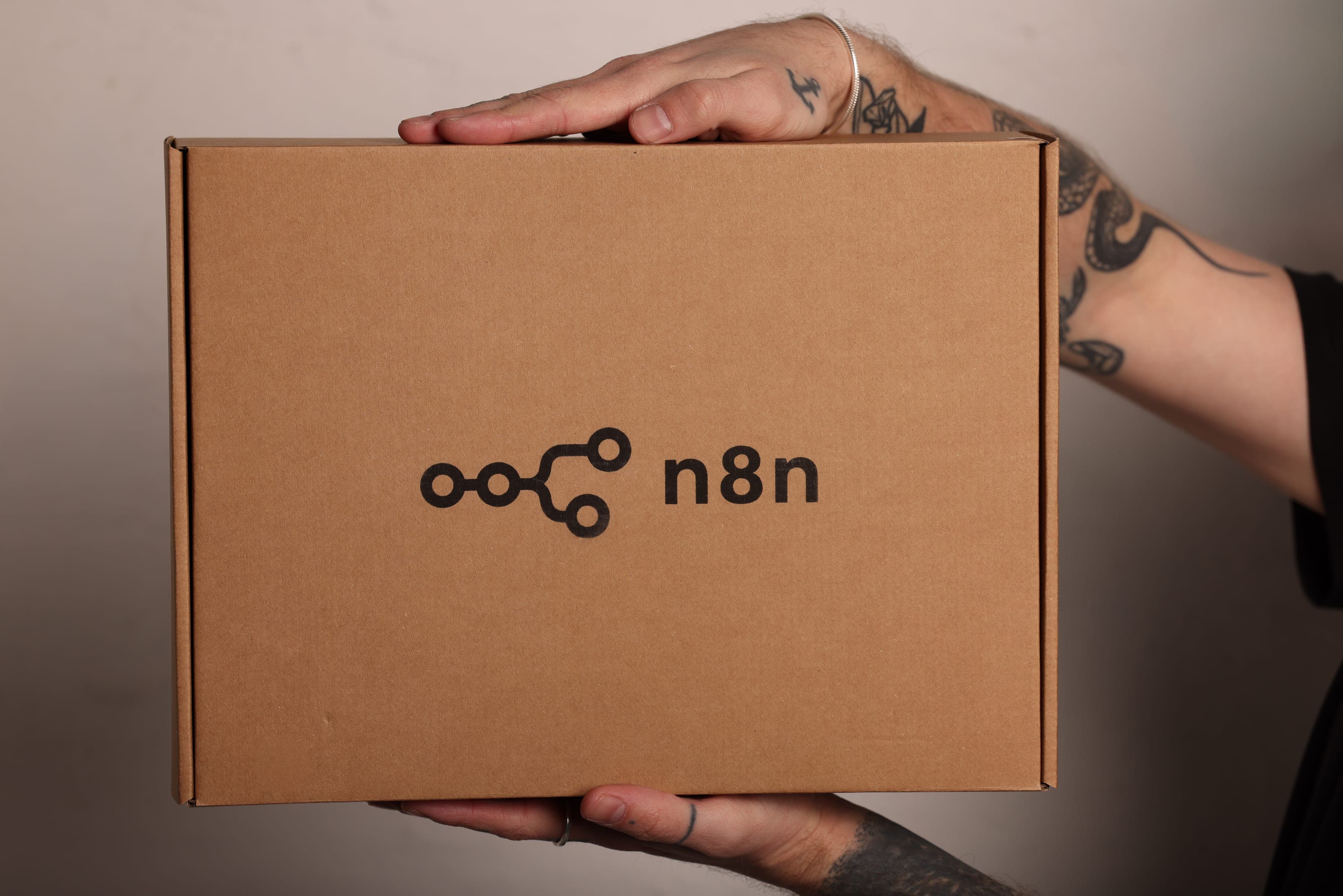 Tattooed hands hold a kraft mailer box printed with the n8n logo