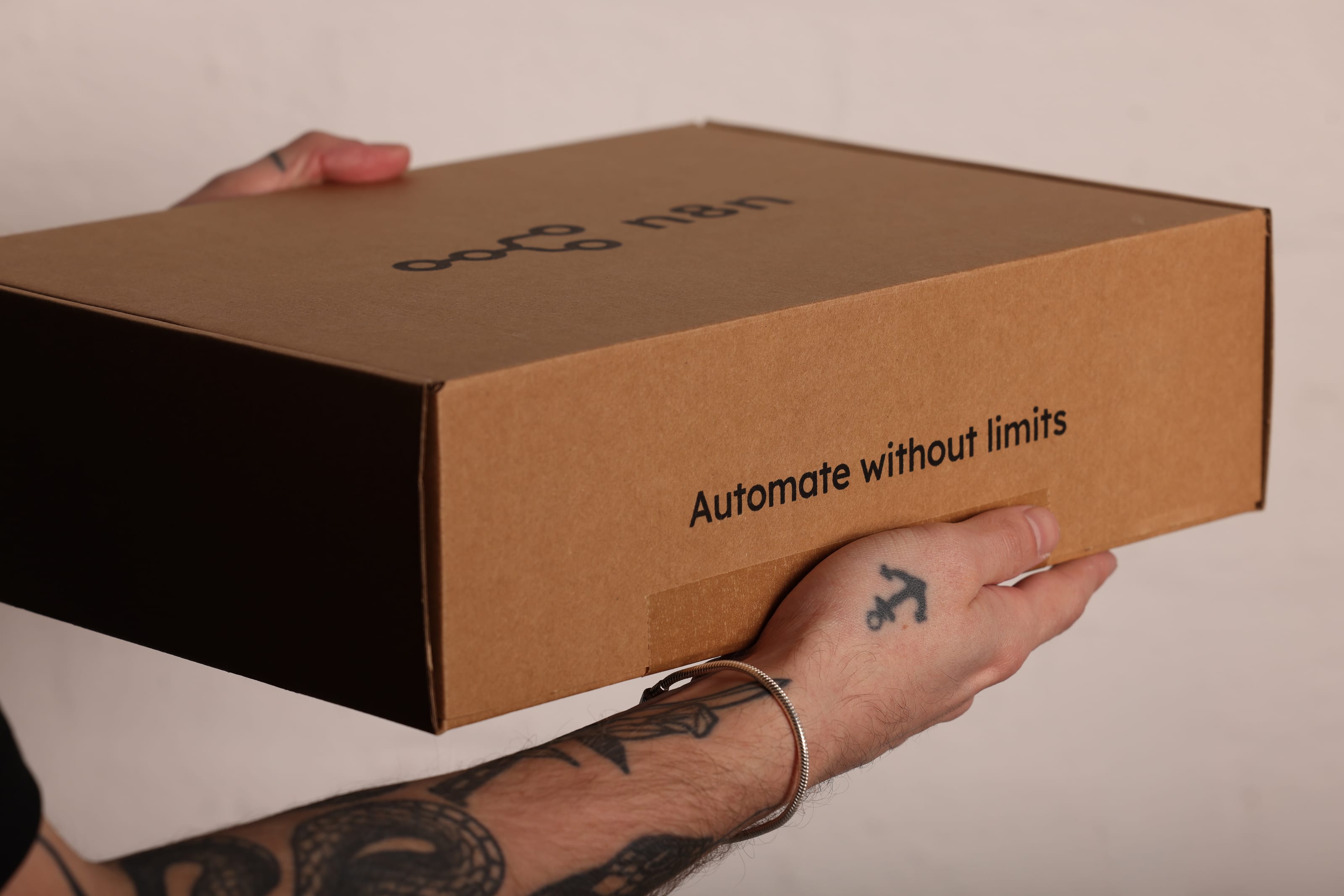 Hands holding a kraft mailer box printed with the n8n logo and “Automate without limits”.