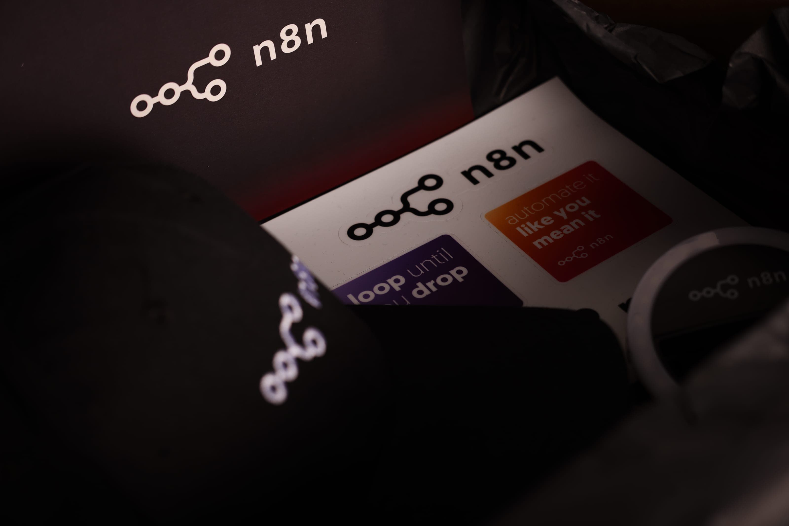An n8n sticker sheet with slogan stickers beside a black n8n cap in a dark box