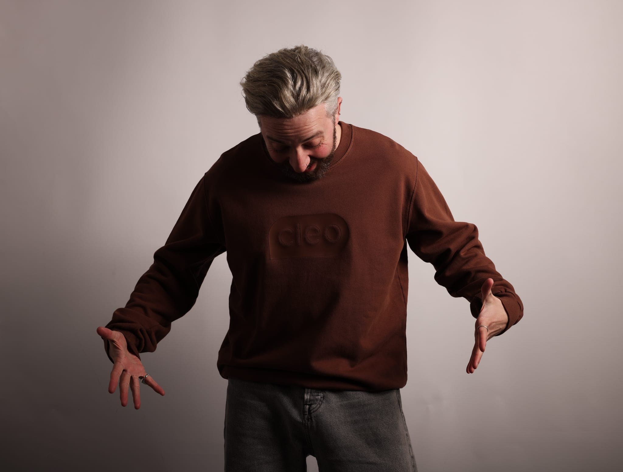 A grey-haired bearded man in a brown sweatshirt with the tonal raised Cleo patch, smiling