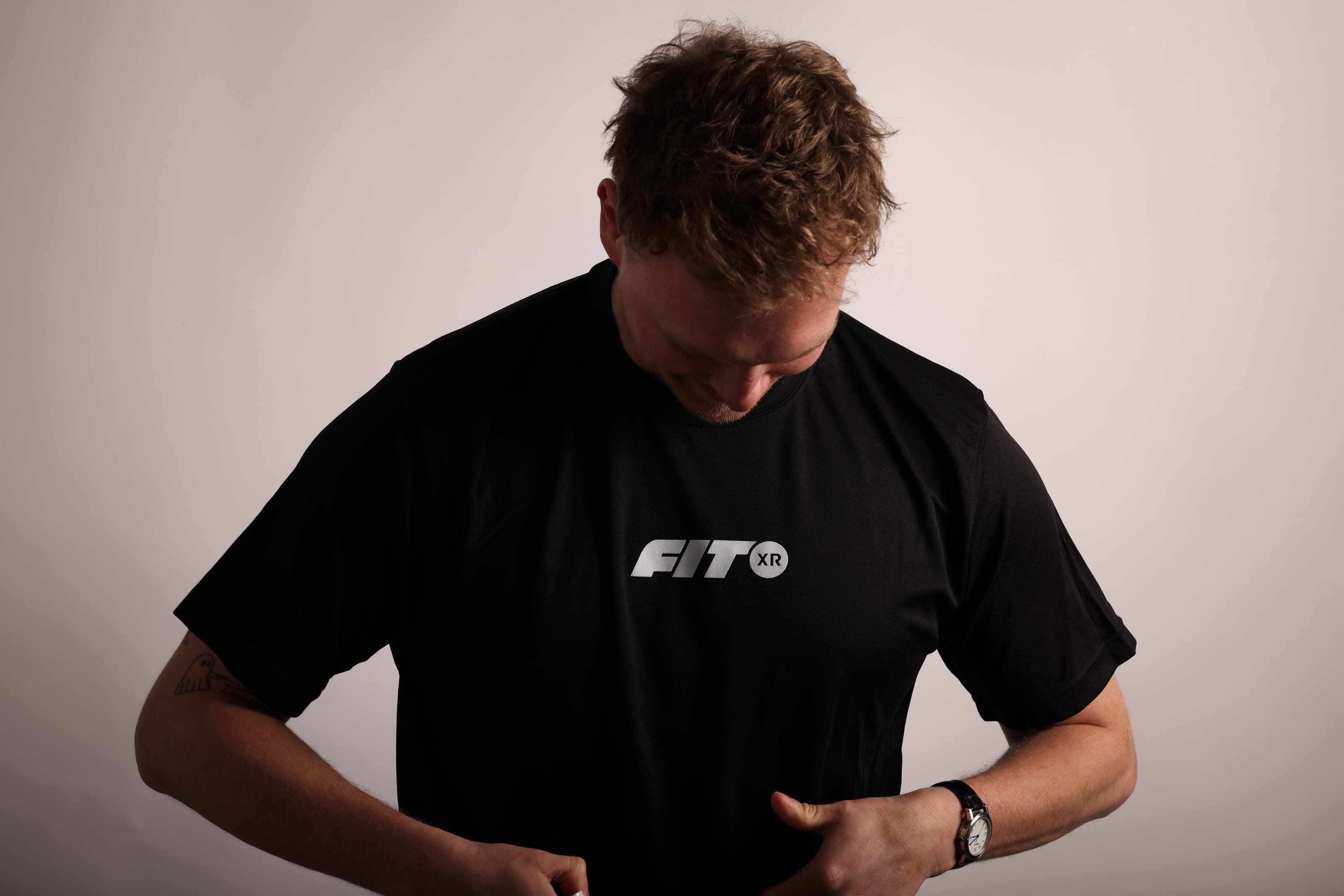 A man looks down at a black FitXR T-shirt, tugging at the hem