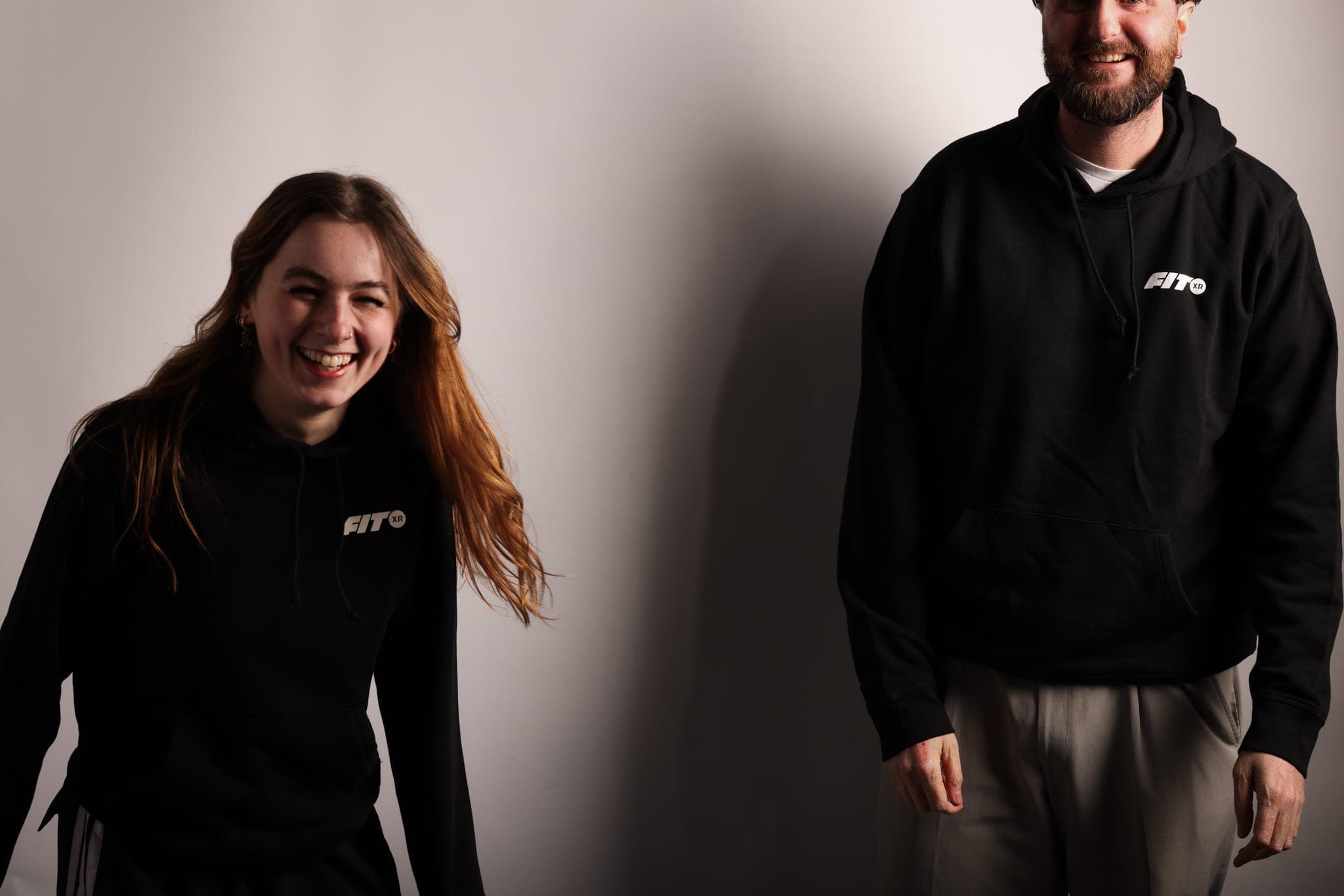 A laughing woman and a smiling bearded man, both in black FitXR hoodies