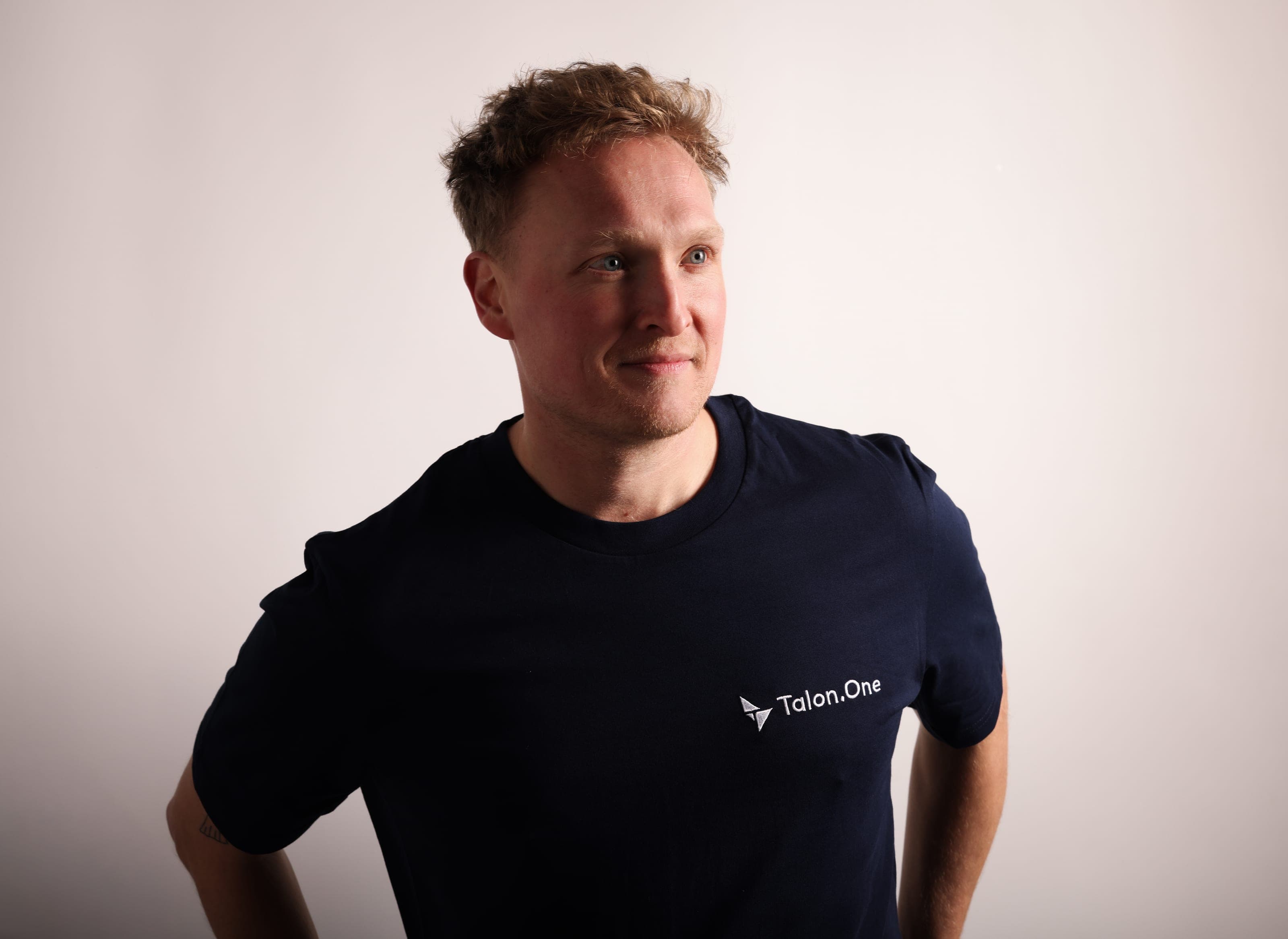A man in a navy Talon.One T-shirt with the white Talon.One logo on the chest, looking to the side