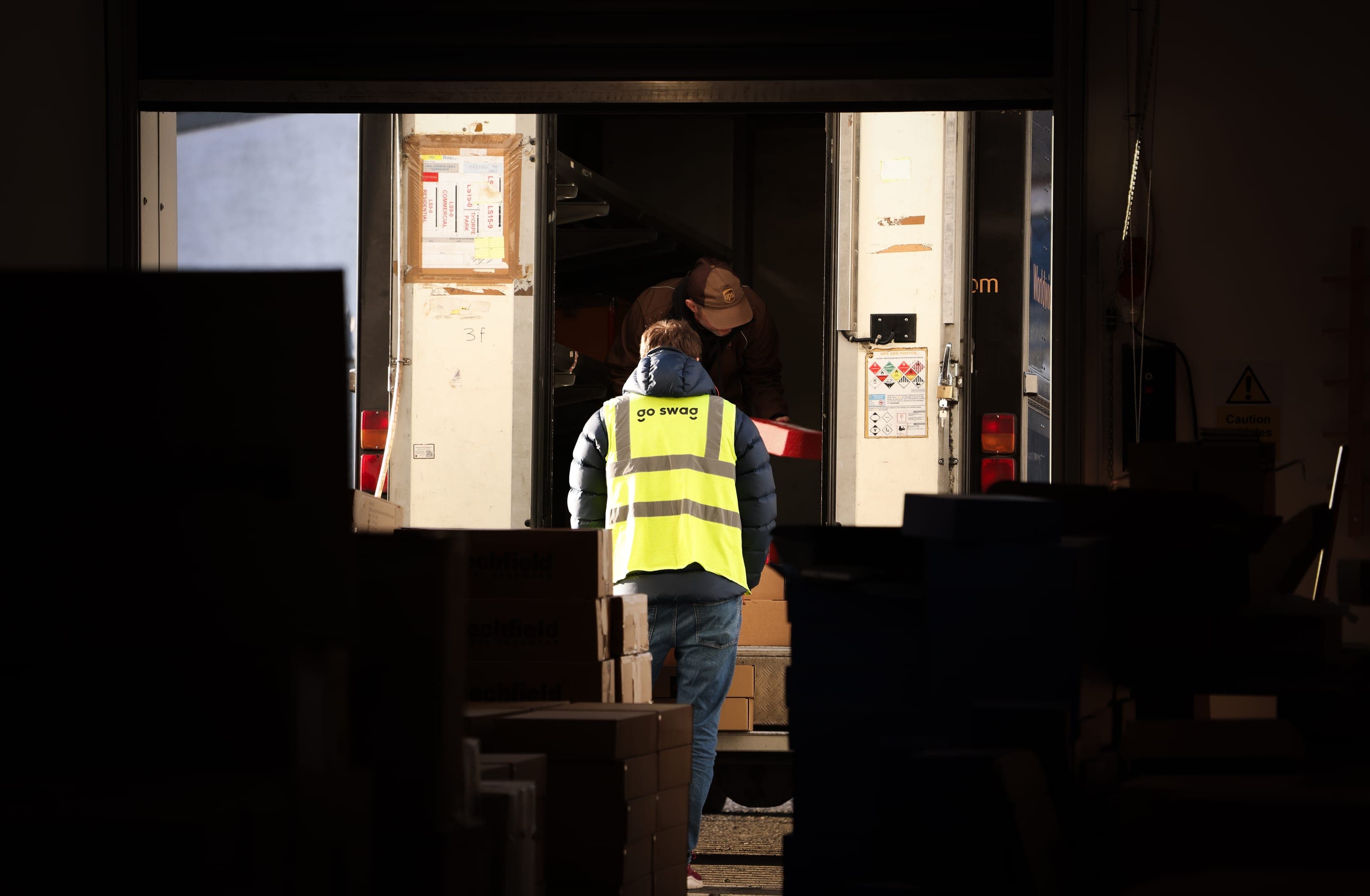 Worker in a Go Swag hi-vis vest at a warehouse door as boxes are loaded into a courier van