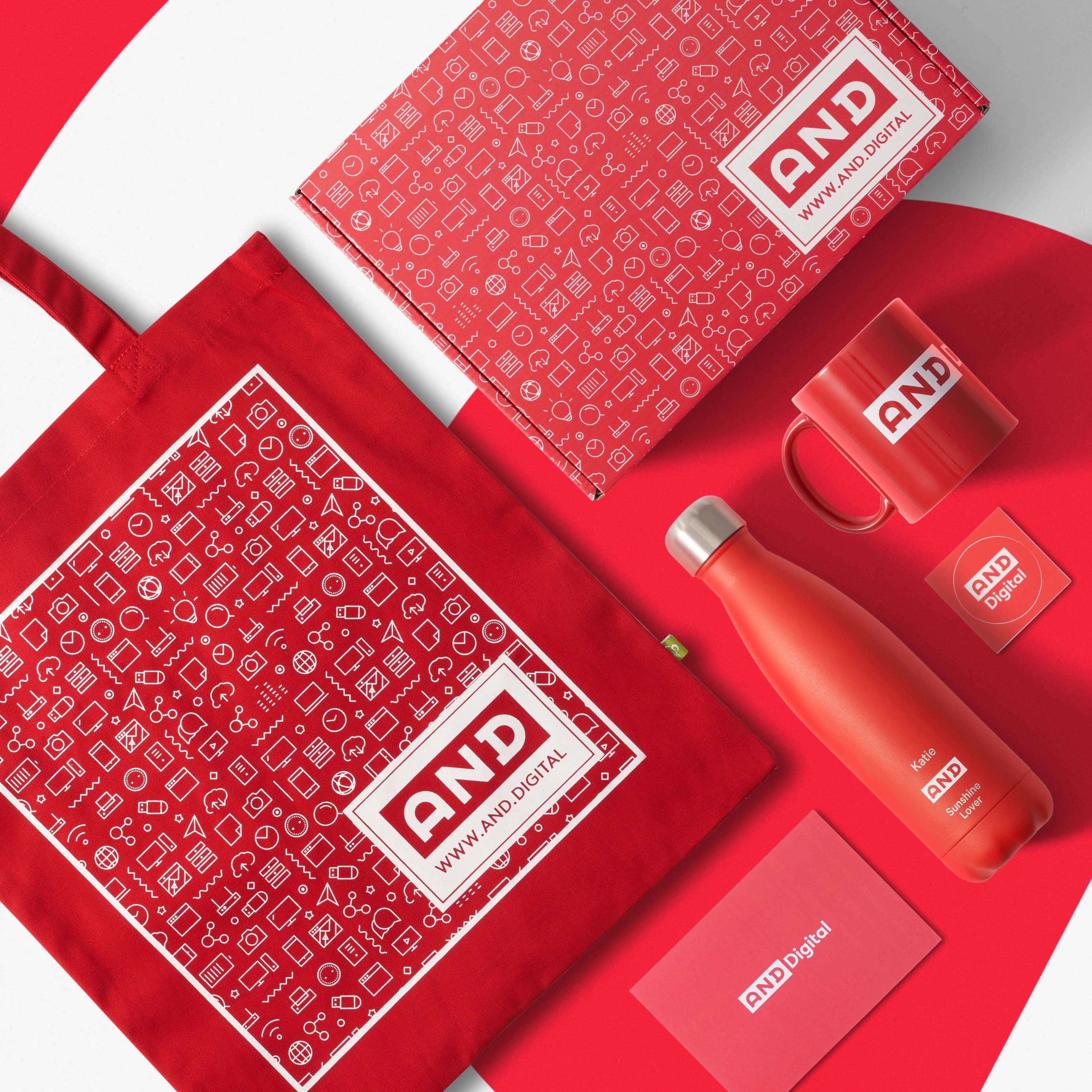 Overhead of a red AND Digital welcome kit: patterned tote, mailer box, mug, personalised bottle, sticker and card