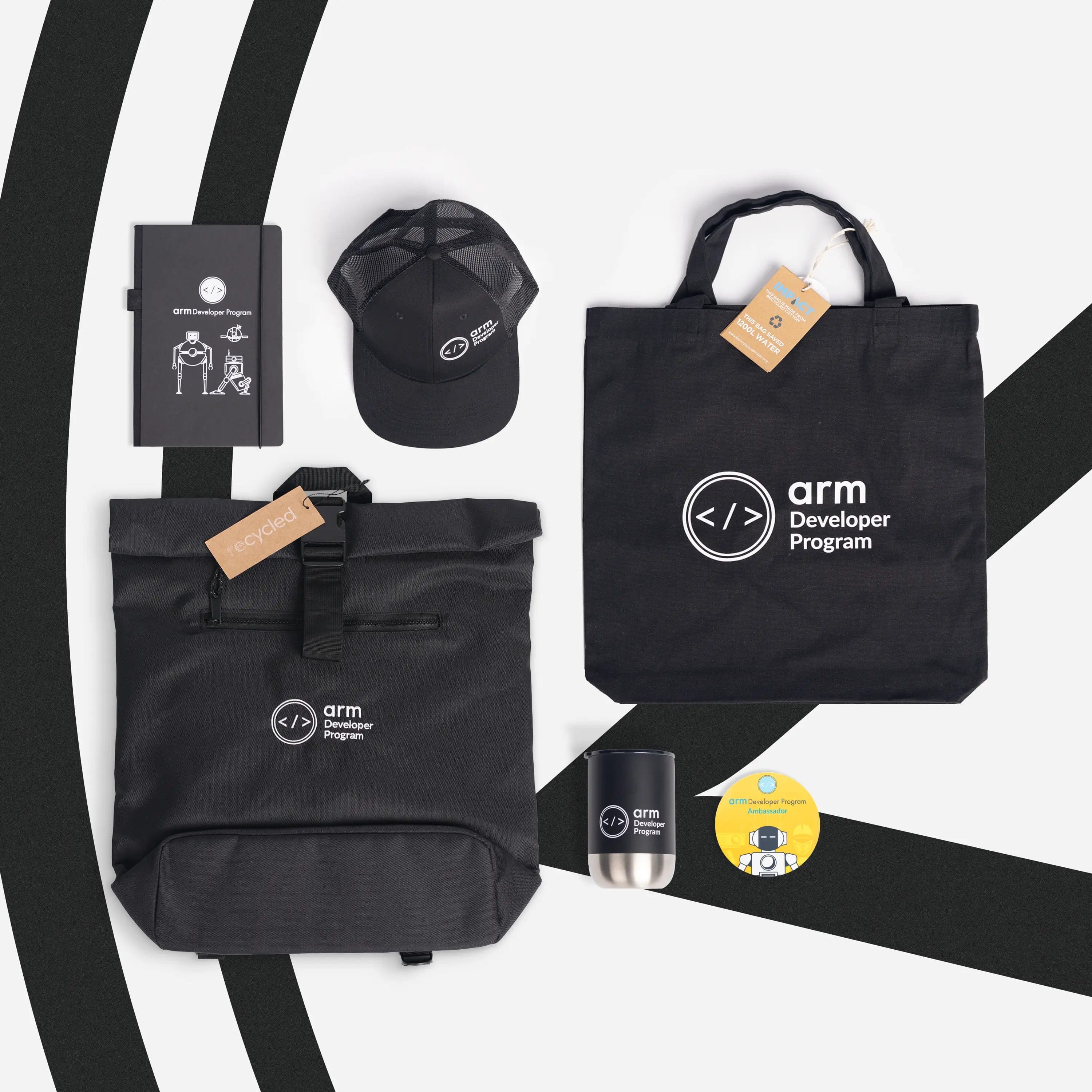Black Arm Developer Program kit from above: roll-top backpack, tote, trucker cap, notebook, tumbler and yellow ambassador badge
