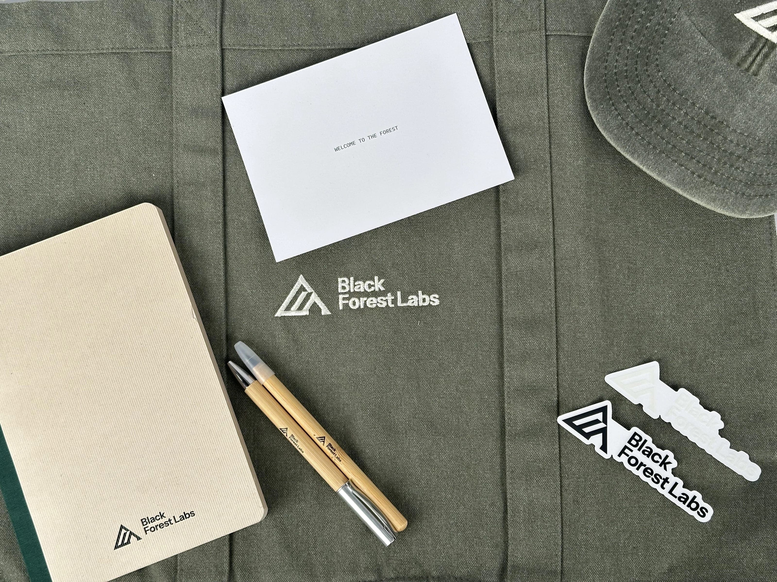 Welcome to the Forest card, cream notebook, bamboo pens and stickers laid on an olive Black Forest Labs tote
