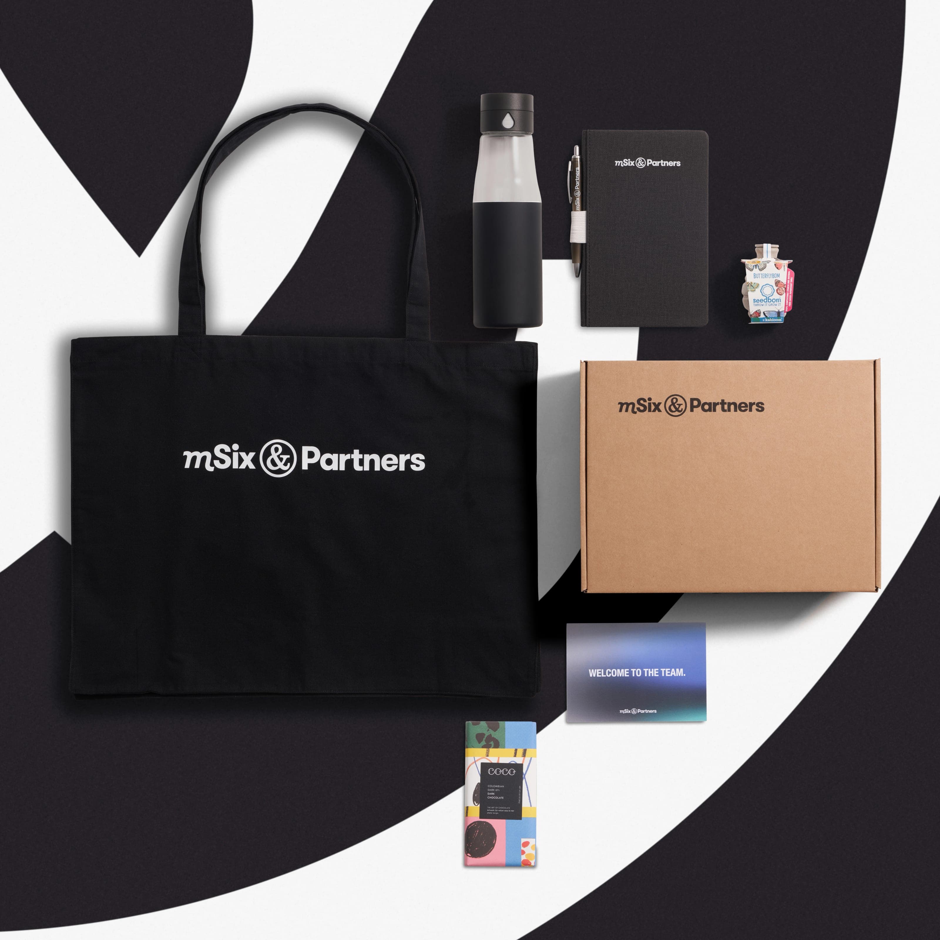 mSix & Partners welcome kit from above: black tote, bottle, notebook and pen, seedbom, kraft box, welcome card and chocolate bar