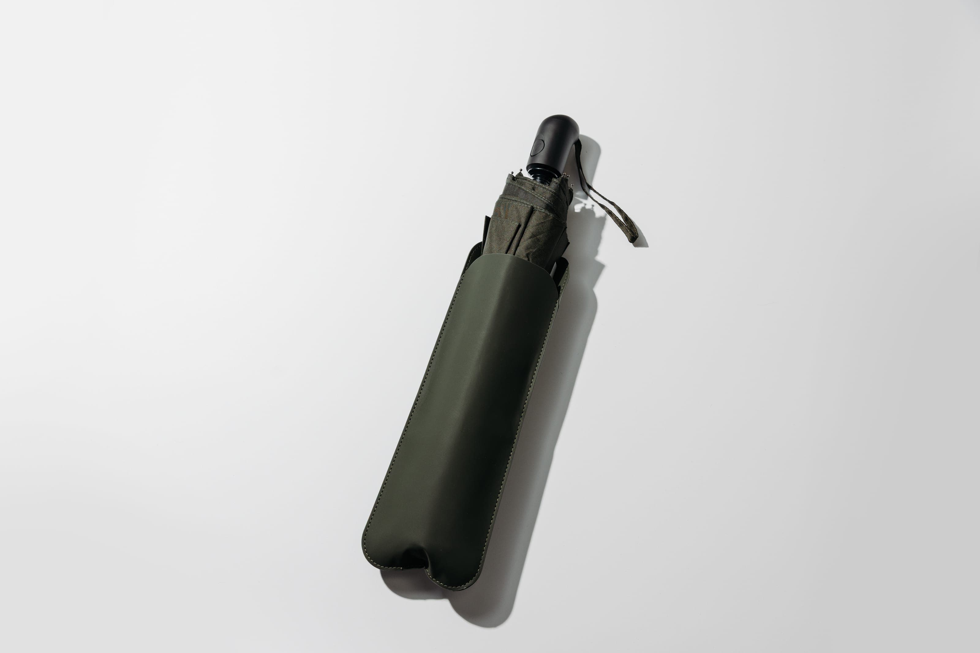 Folded olive umbrella in a matching sleeve on a white surface