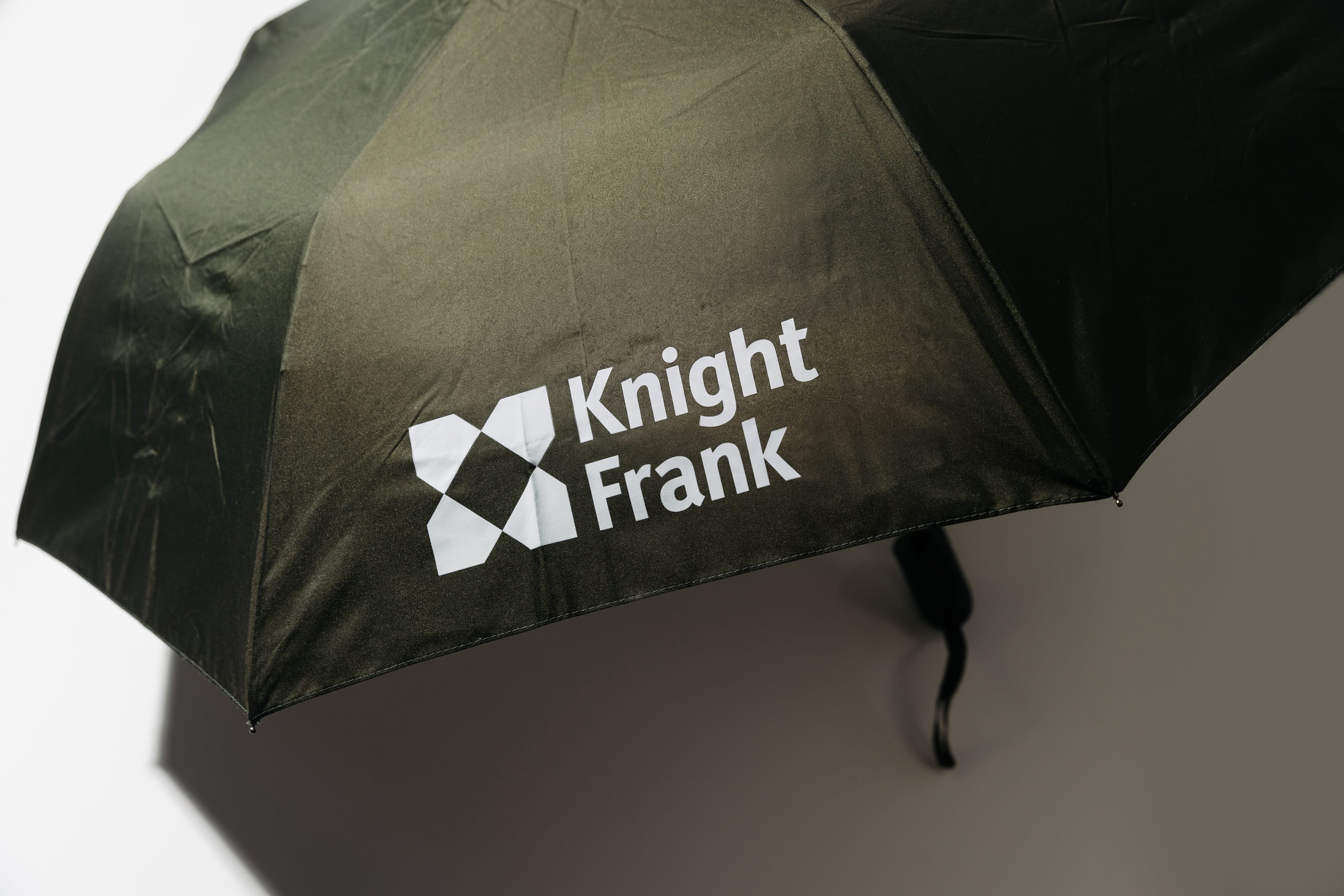 Open olive umbrella printed with the white Knight Frank logo.