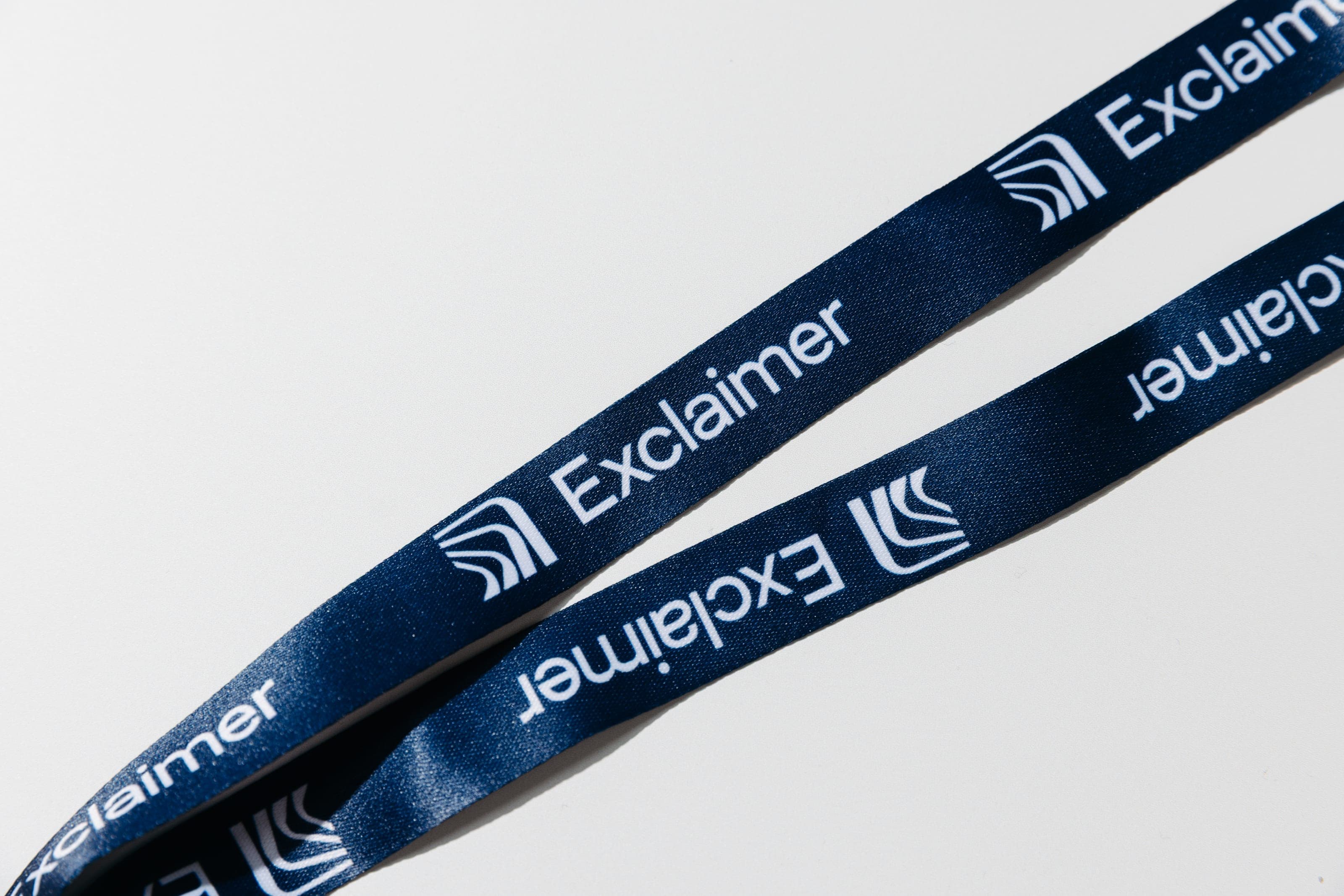 Navy lanyard printed with repeating white Exclaimer logos on a white surface