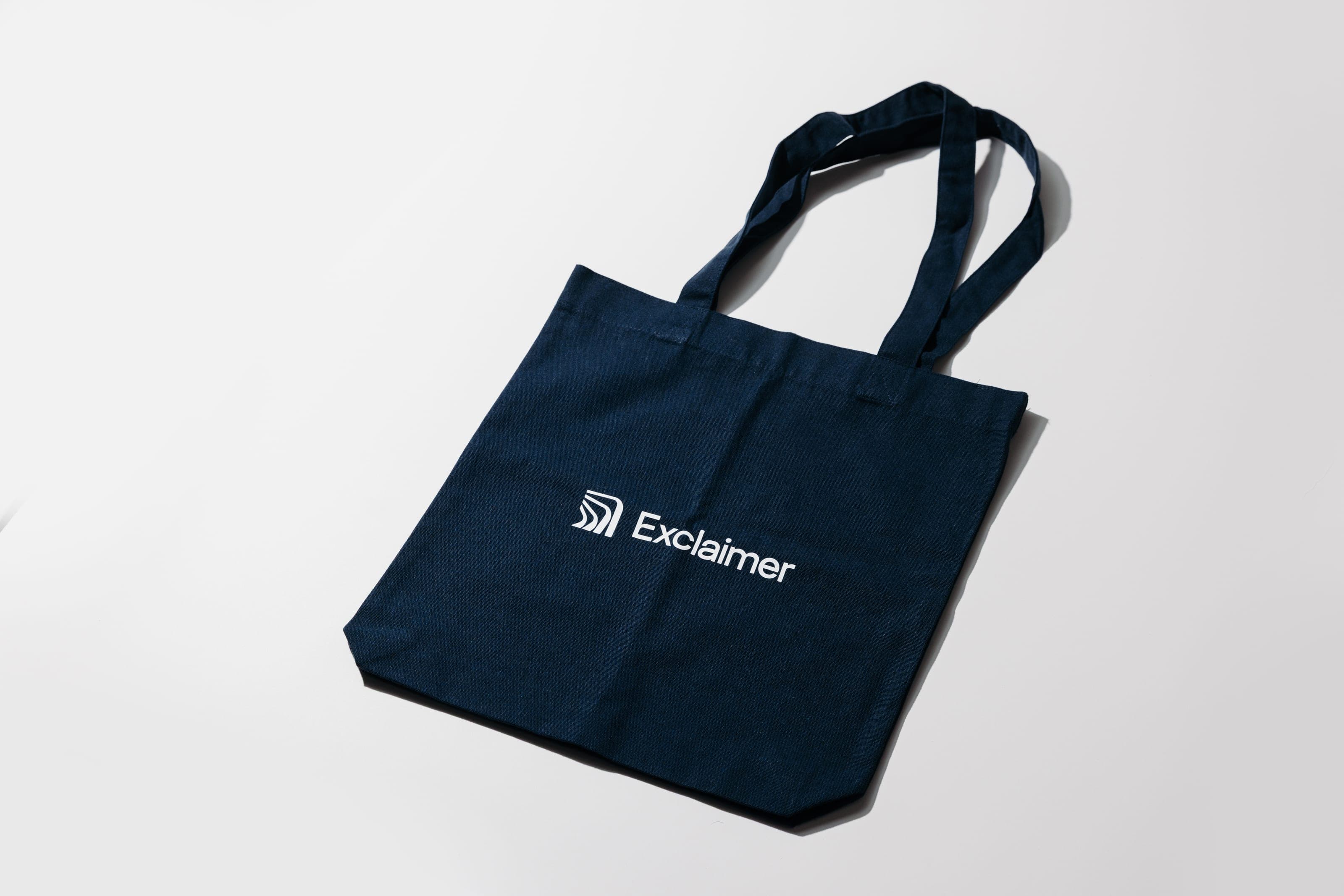 Navy canvas tote bag printed with the white Exclaimer logo on a white surface