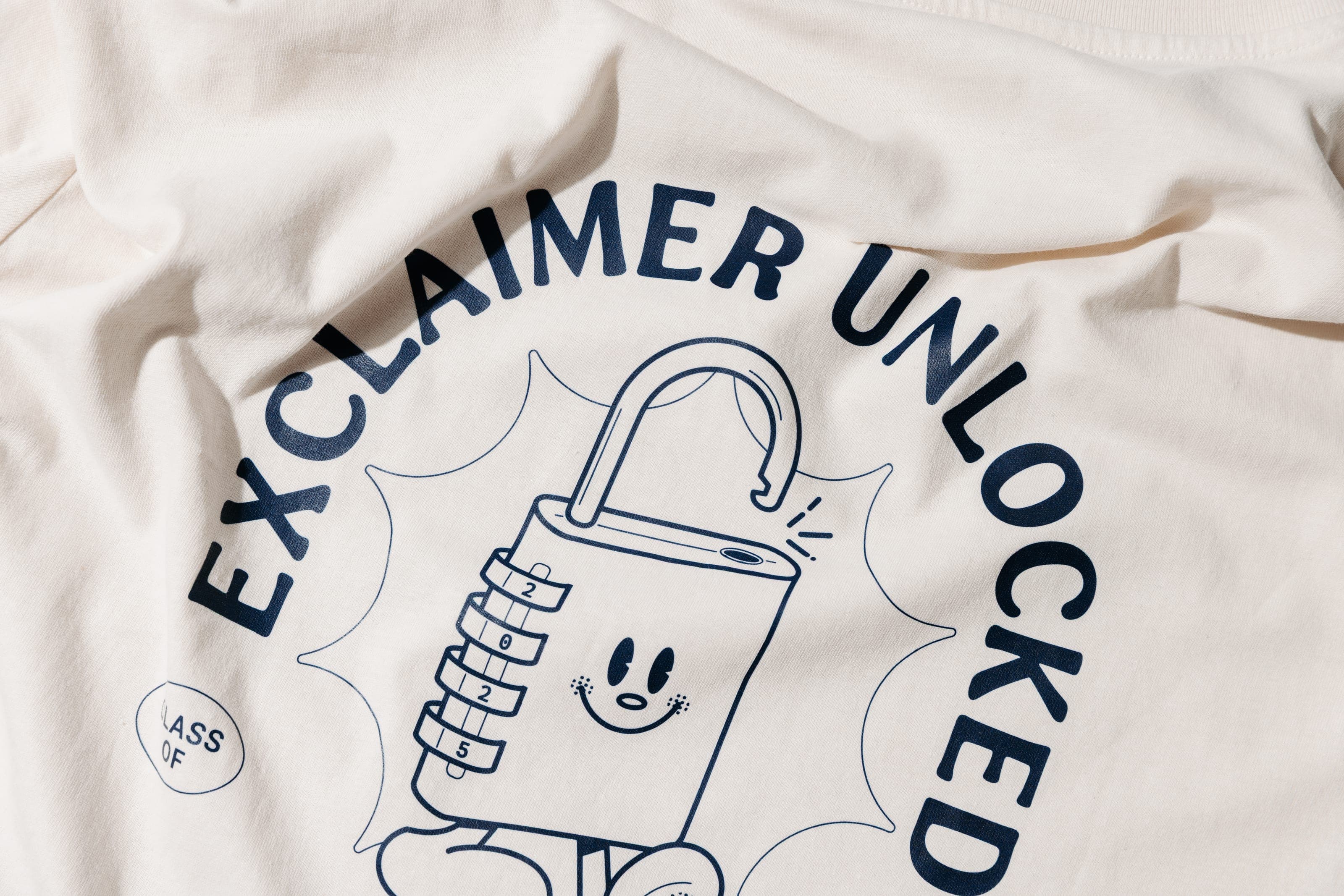 Close-up of a smiling padlock character and 'Exclaimer Unlocked' printed in navy on cream cotton
