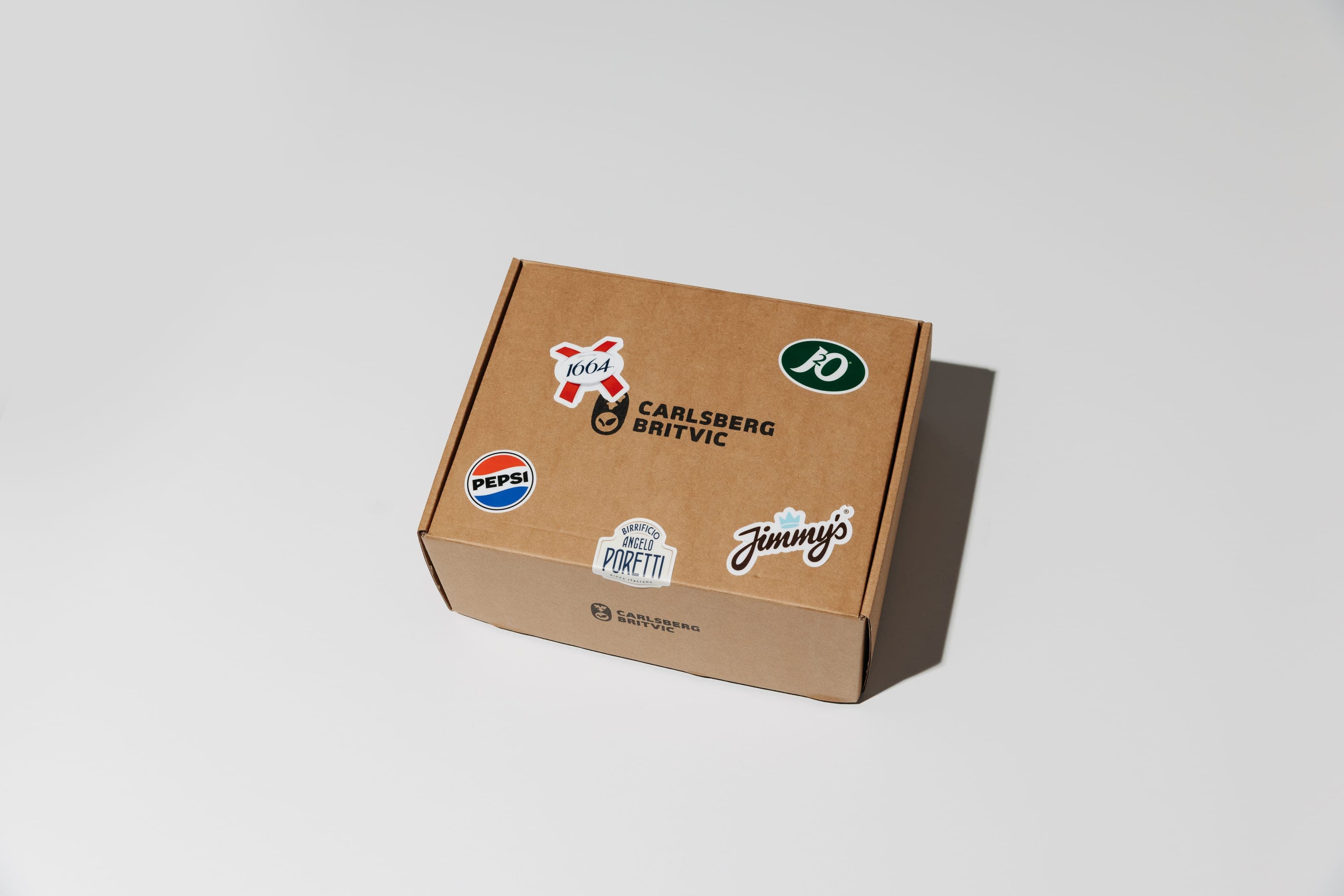 A closed kraft mailer box printed with the Carlsberg Britvic logo and covered in drinks-brand stickers