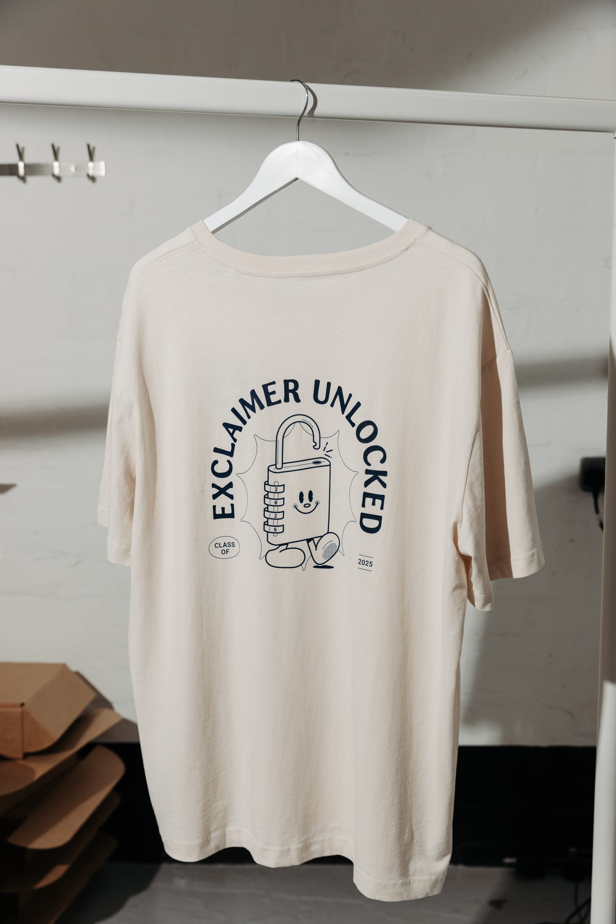 Back of a cream T-shirt printed with Exclaimer Unlocked, a padlock character and Class of 2025