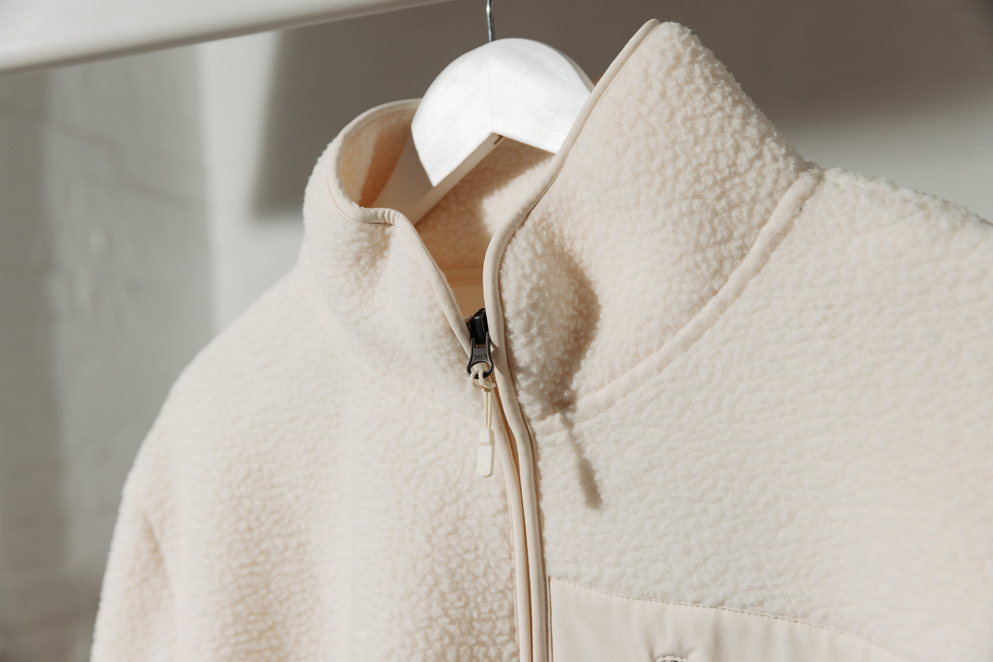Cream sherpa fleece with a stand collar and zip on a white hanger