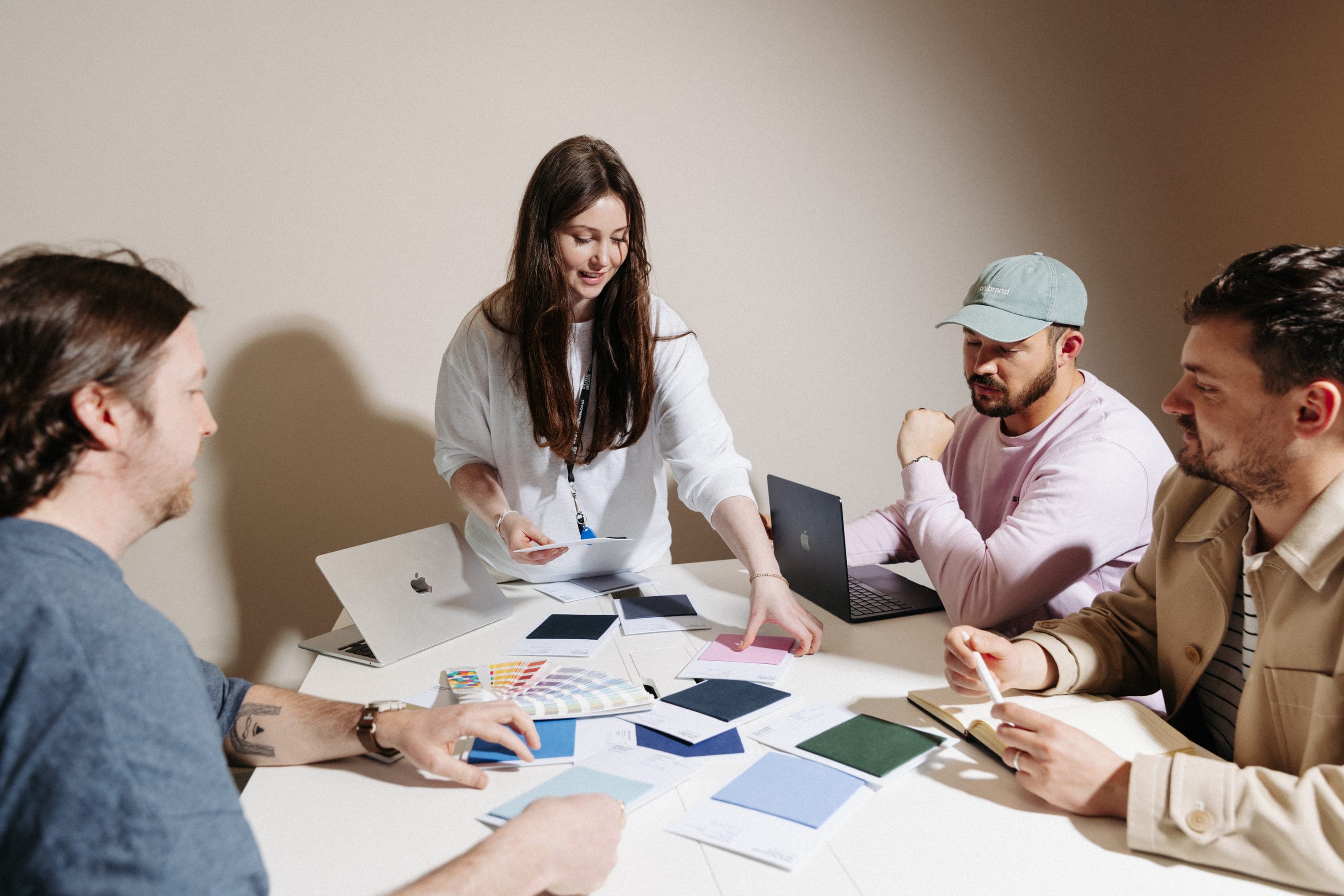 Woman presenting colour swatches to three colleagues around a white table with laptops