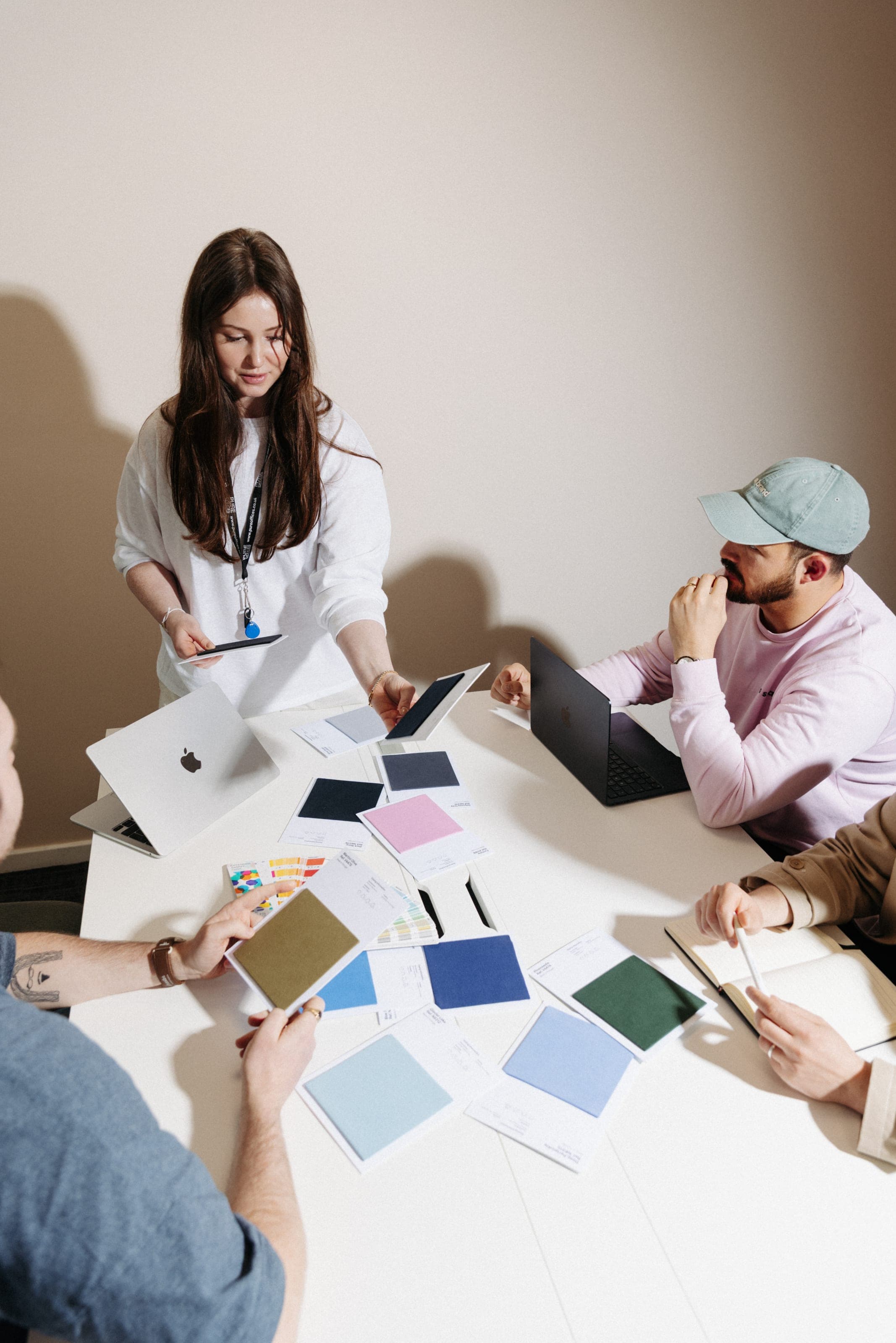 Woman in white presenting colour swatches across a meeting table to seated colleagues