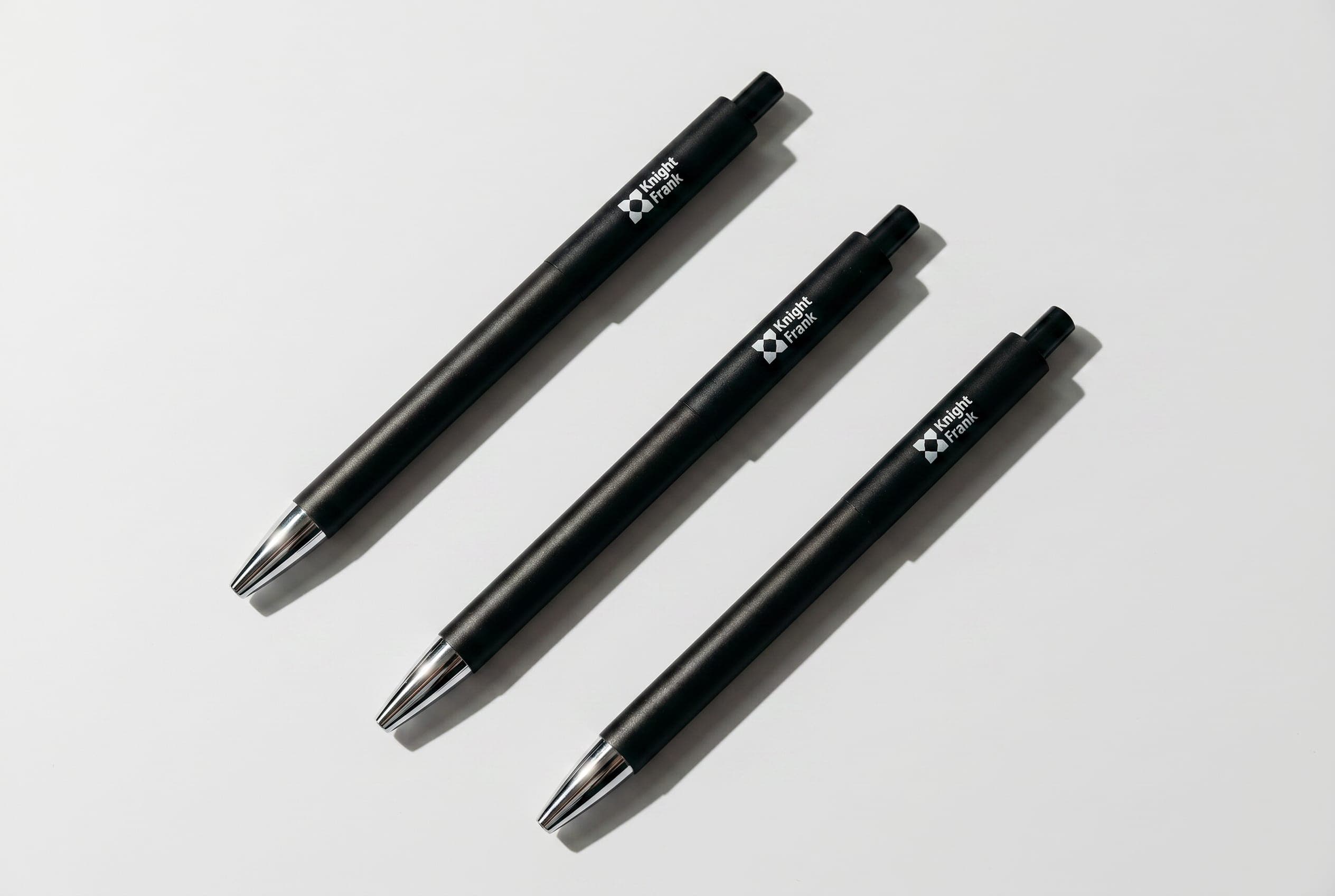 Three black pens with chrome tips and the white Knight Frank logo lying diagonally on pale grey