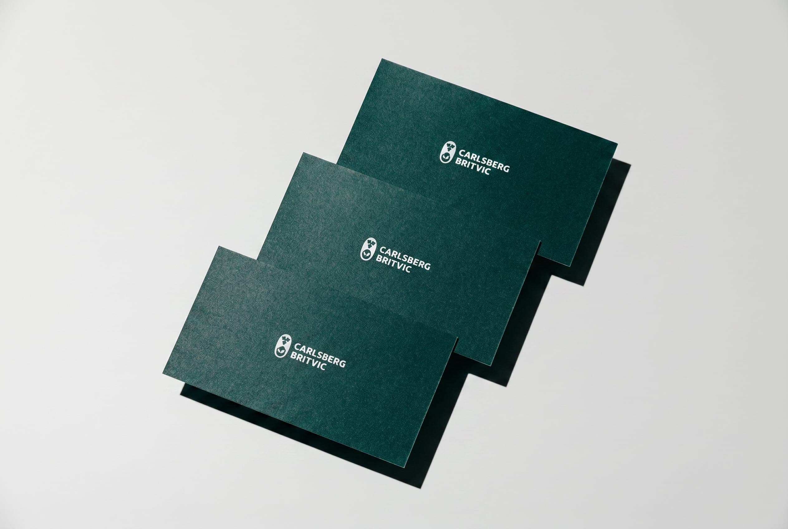 Three dark green Carlsberg Britvic cards fanned on a pale grey surface