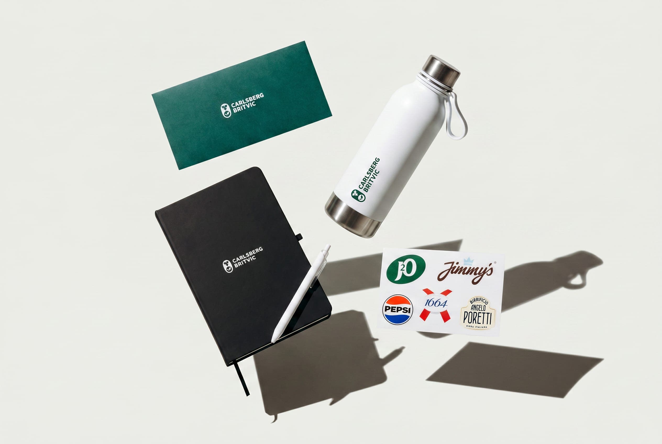 Carlsberg Britvic green card, black notebook, white bottle and brand sticker sheet floating over white