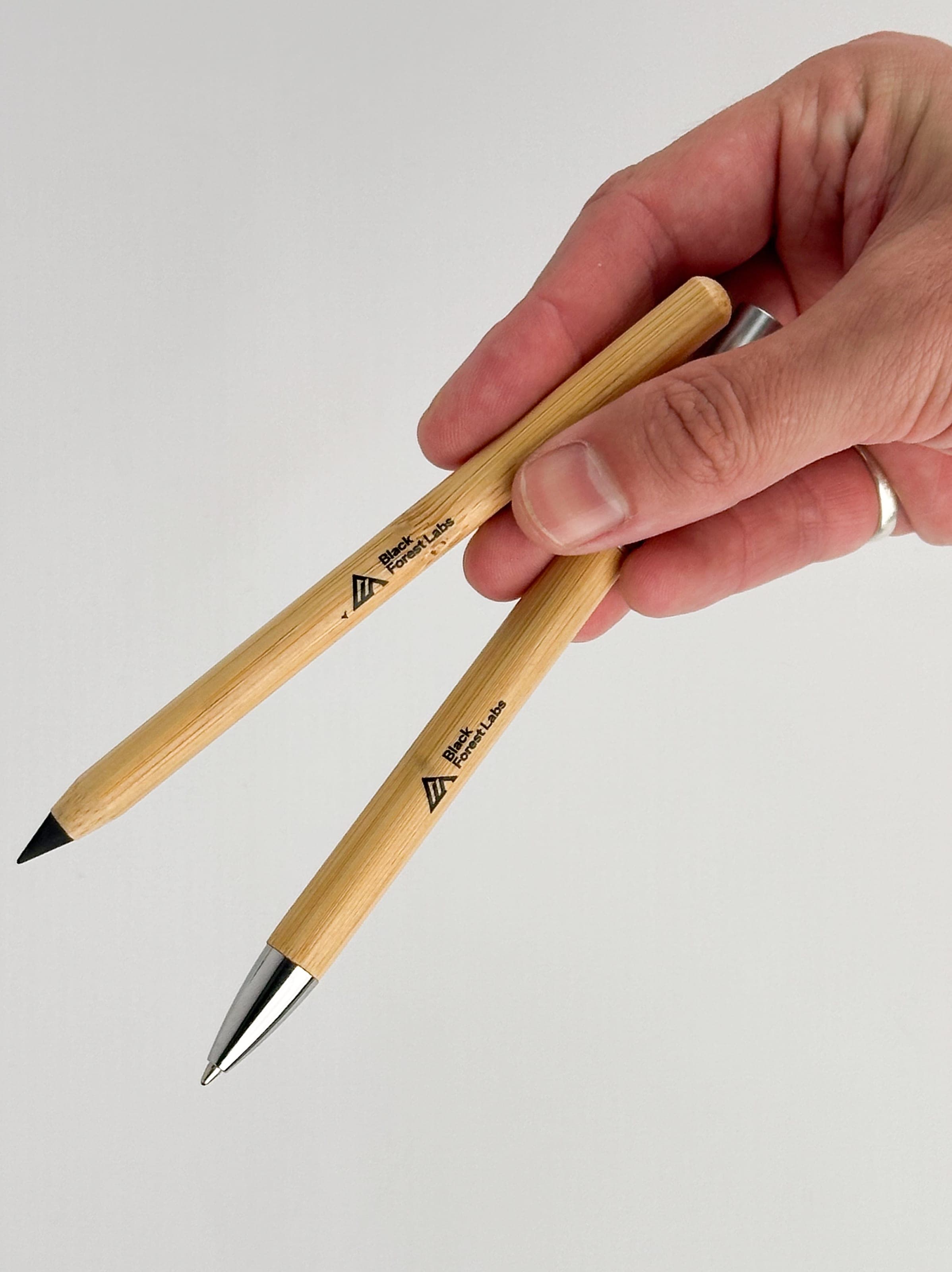 A hand holding a bamboo pencil and a bamboo pen, both printed with the Black Forest Labs logo
