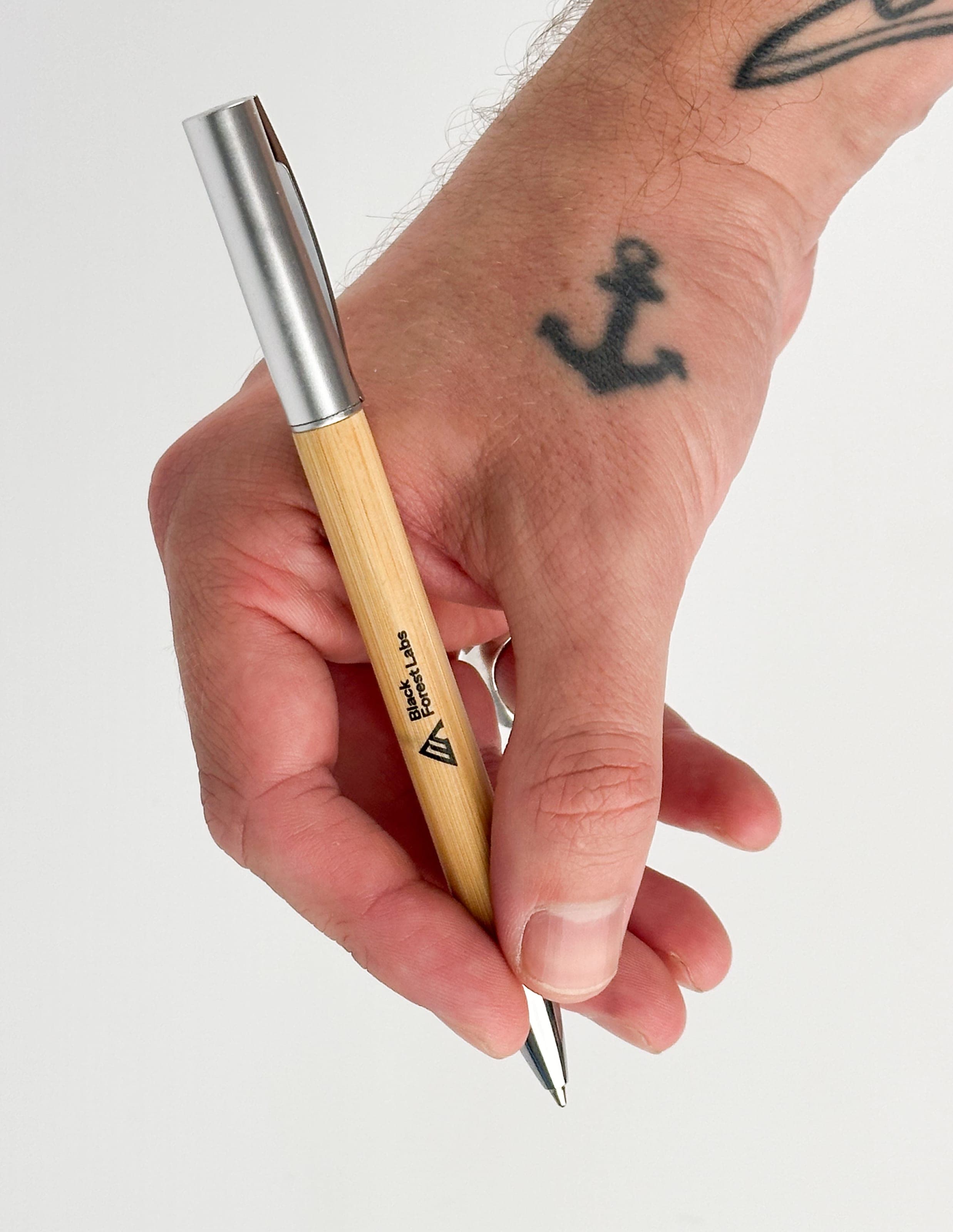 A tattooed hand gripping a bamboo pen with a silver cap printed with the Black Forest Labs logo
