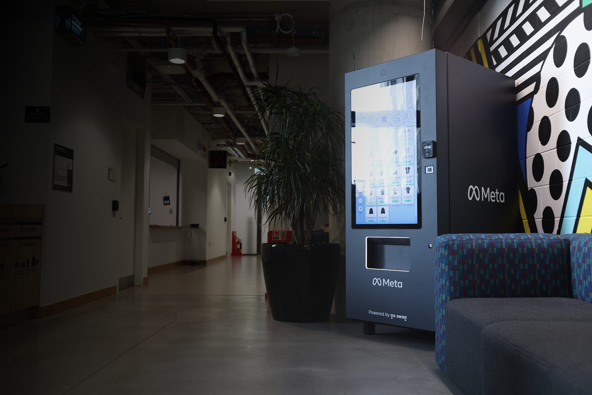 A lit, Meta-branded vending machine, marked “Powered by go swag”, beside a mural at the end of a dim corridor.
